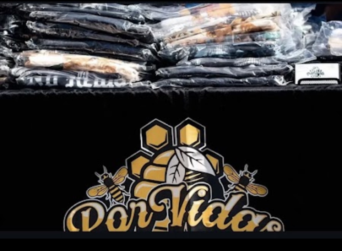 Stacked packages above a black sign with honeycomb and bee illustrations, and the text 'Dar Vida'.