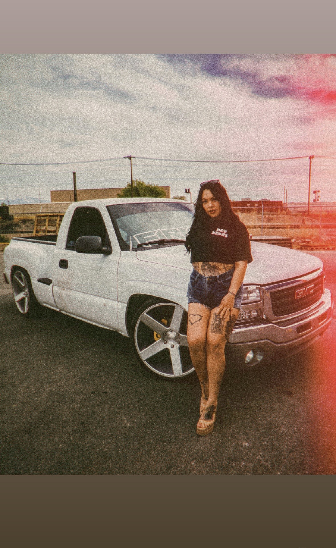 Woman standing next to a white pickup truck outdoors, with a cloudy sky and power lines in the background.