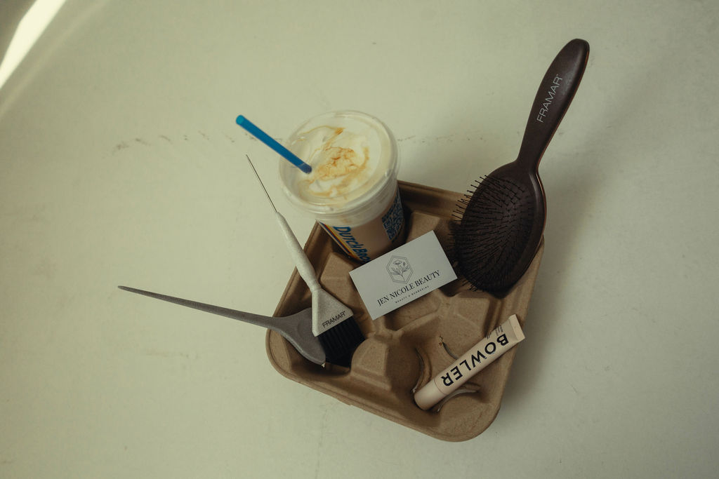 Tray with a cup of whipped cream, a black hairbrush, a business card, and a small tube on a light surface.