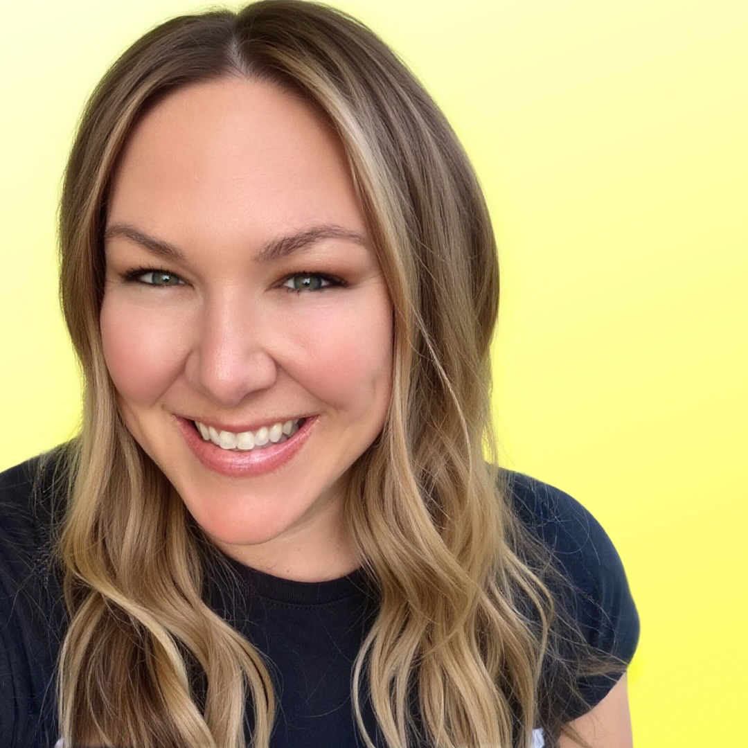 Smiling woman with long wavy hair against yellow background.