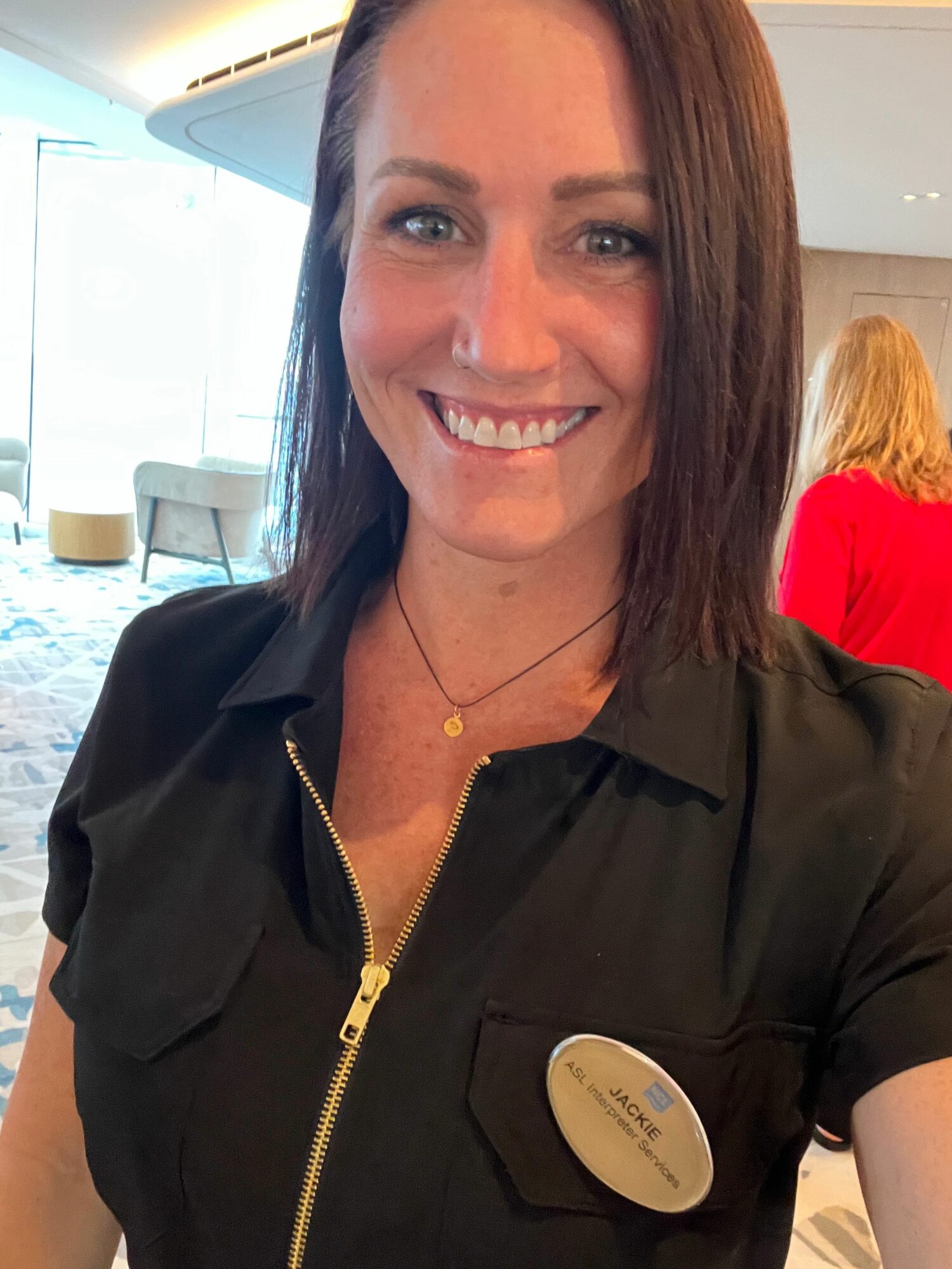 Smiling woman with dark hair, wearing a black top with a gold zipper, in an indoor setting.