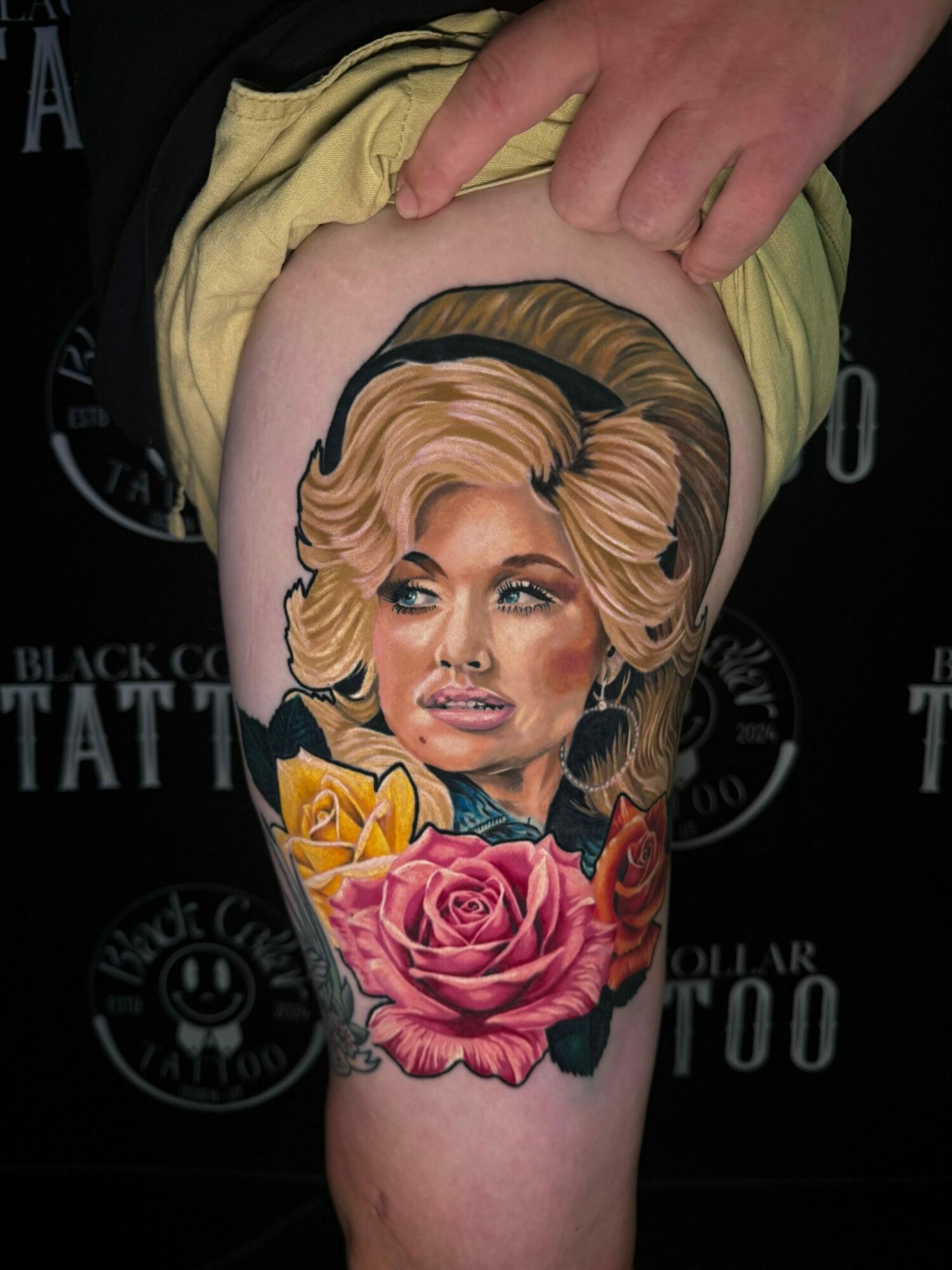 Colorful tattoo of a woman with blonde hair, pink roses, and yellow ribbon on upper arm, viewed sideways.
