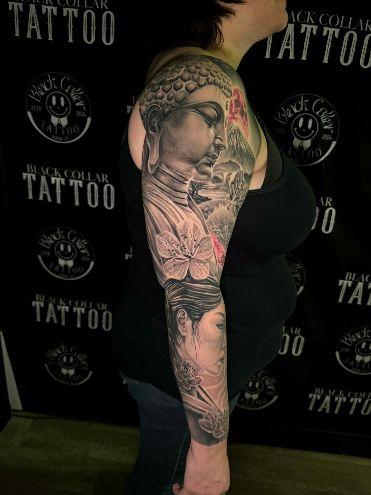 Side view of a person with a detailed tattoo sleeve on their arm, standing against a black background with logos.