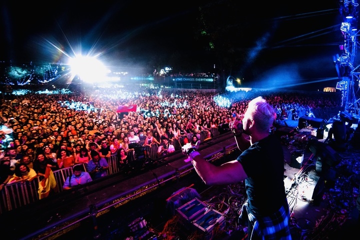DJ performing on stage with a large crowd at night, bright lights illuminating the scene.