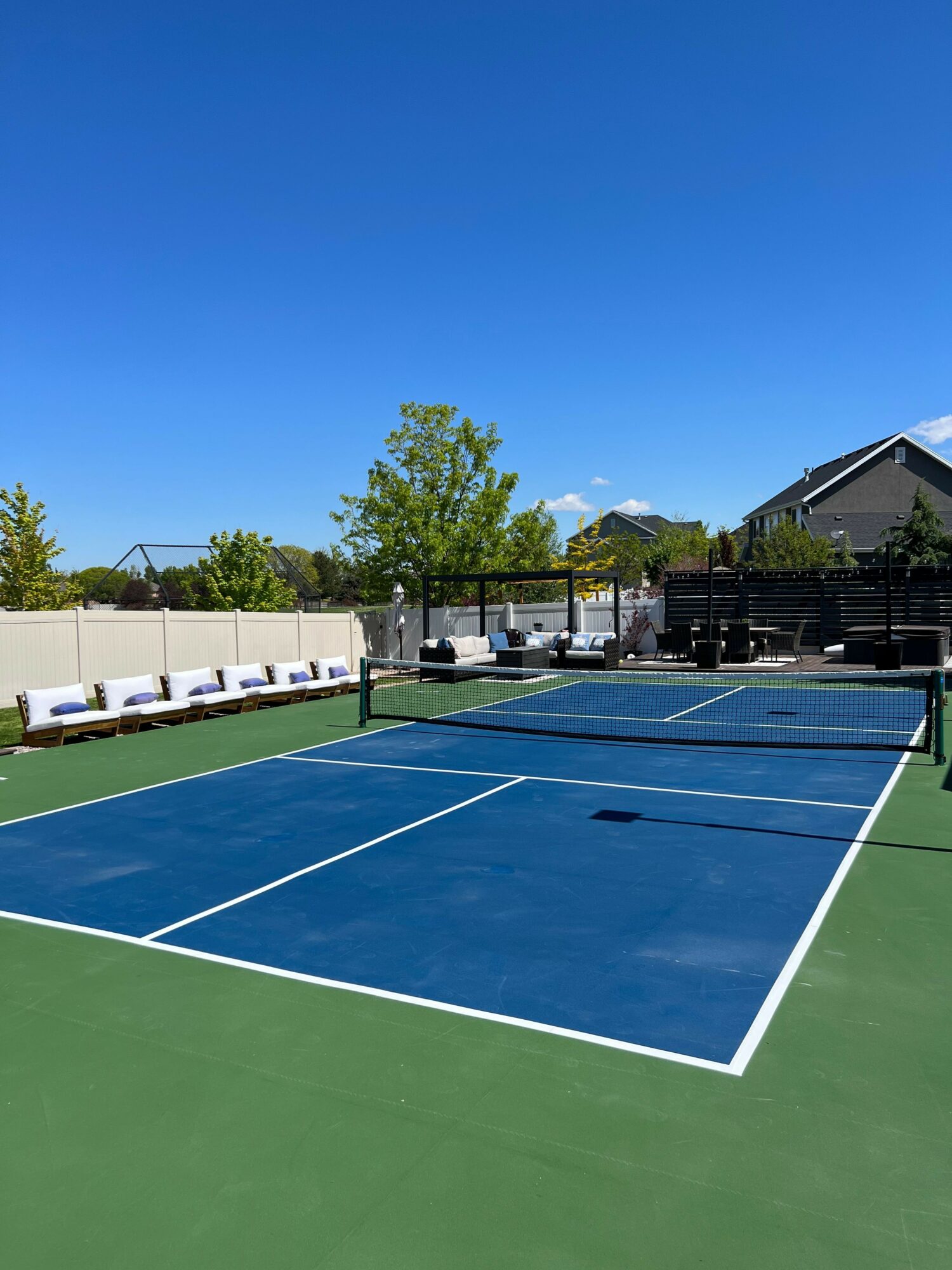 Tennis court with blue and green surface, surrounded by trees and a building, under a clear blue sky.