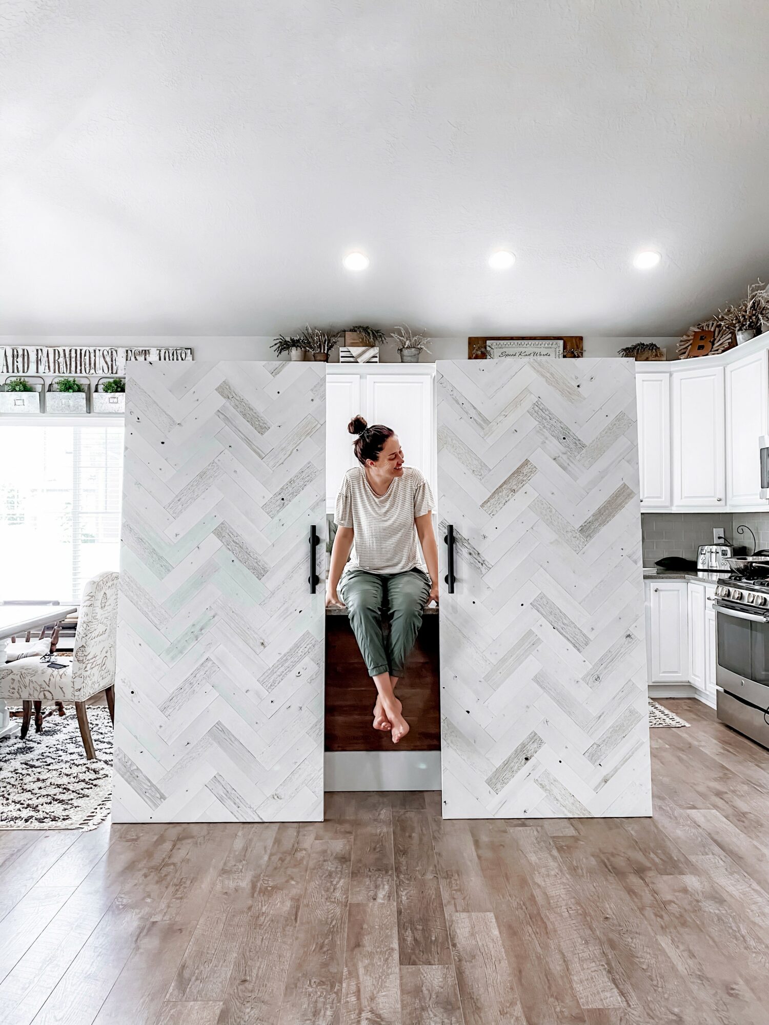 Person sitting on a small platform inside a large, white, herringbone-patterned structure in a kitchen, with a living area visible to the left.