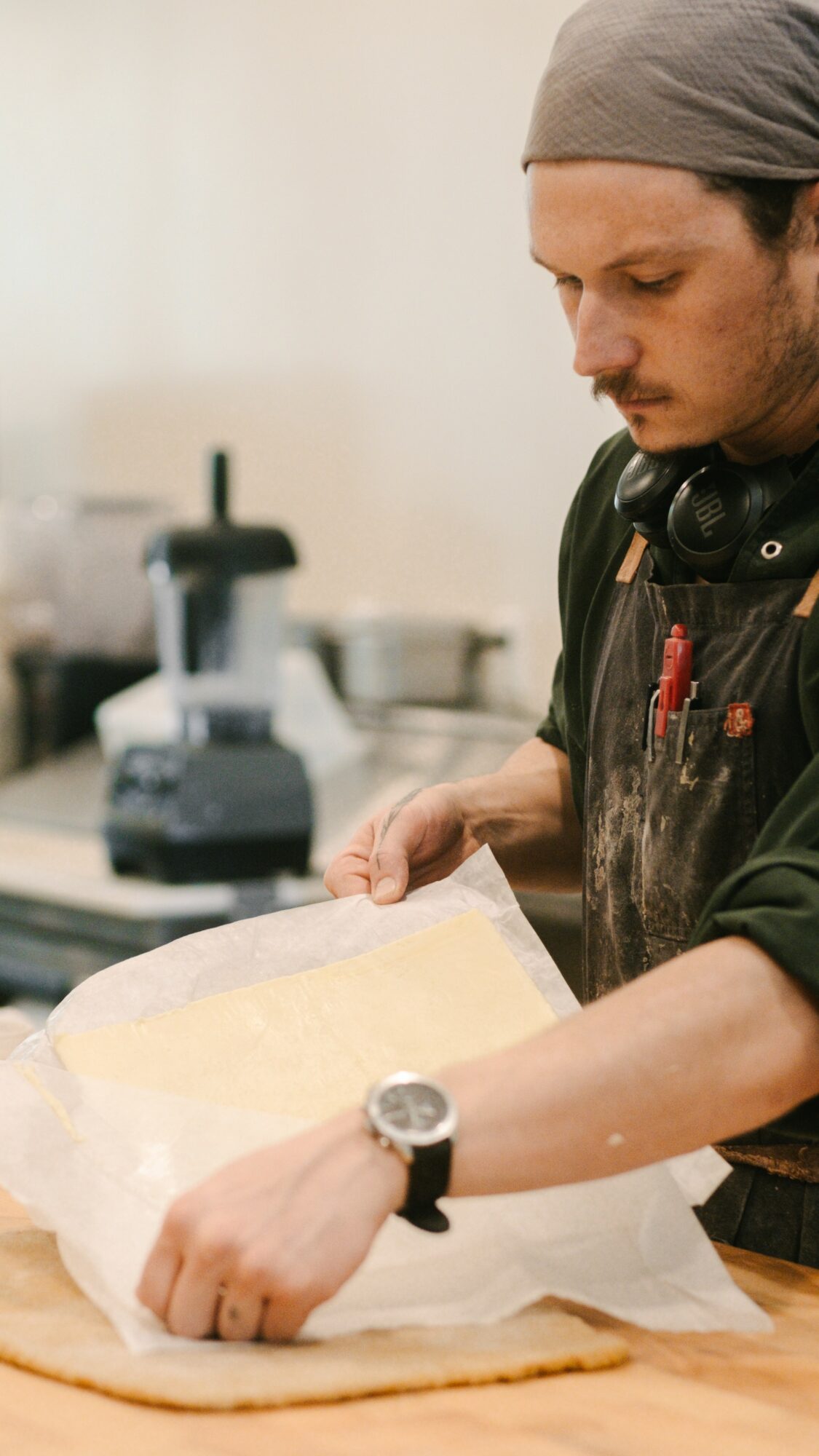 Person wearing a head covering and apron preparing dough on a wooden surface in a kitchen.