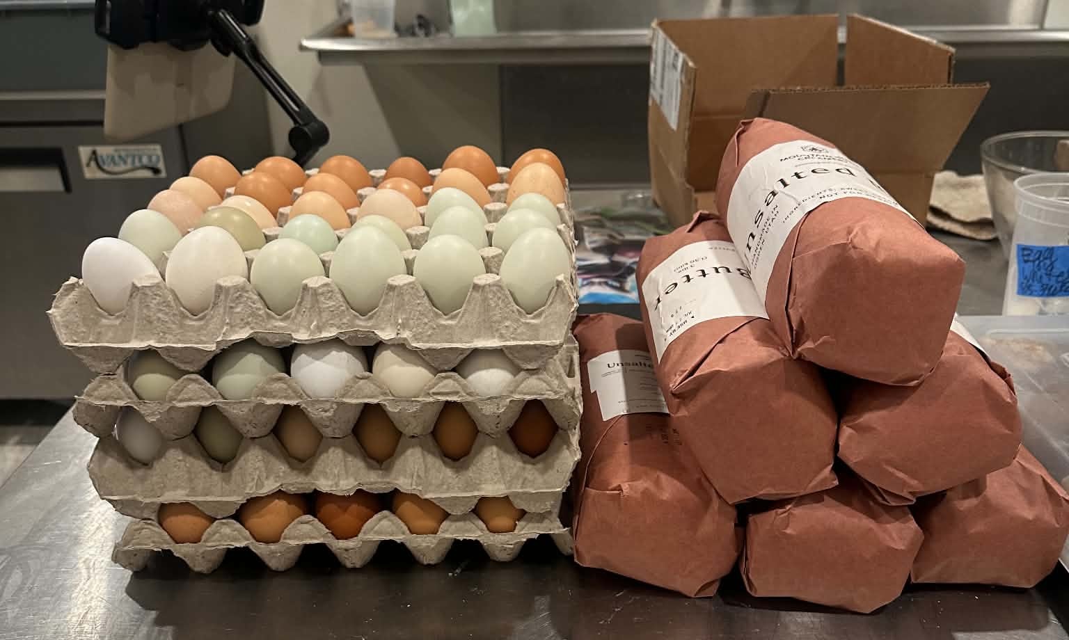 Multiple cartons of eggs and wrapped packages on a table, with a cardboard box nearby.