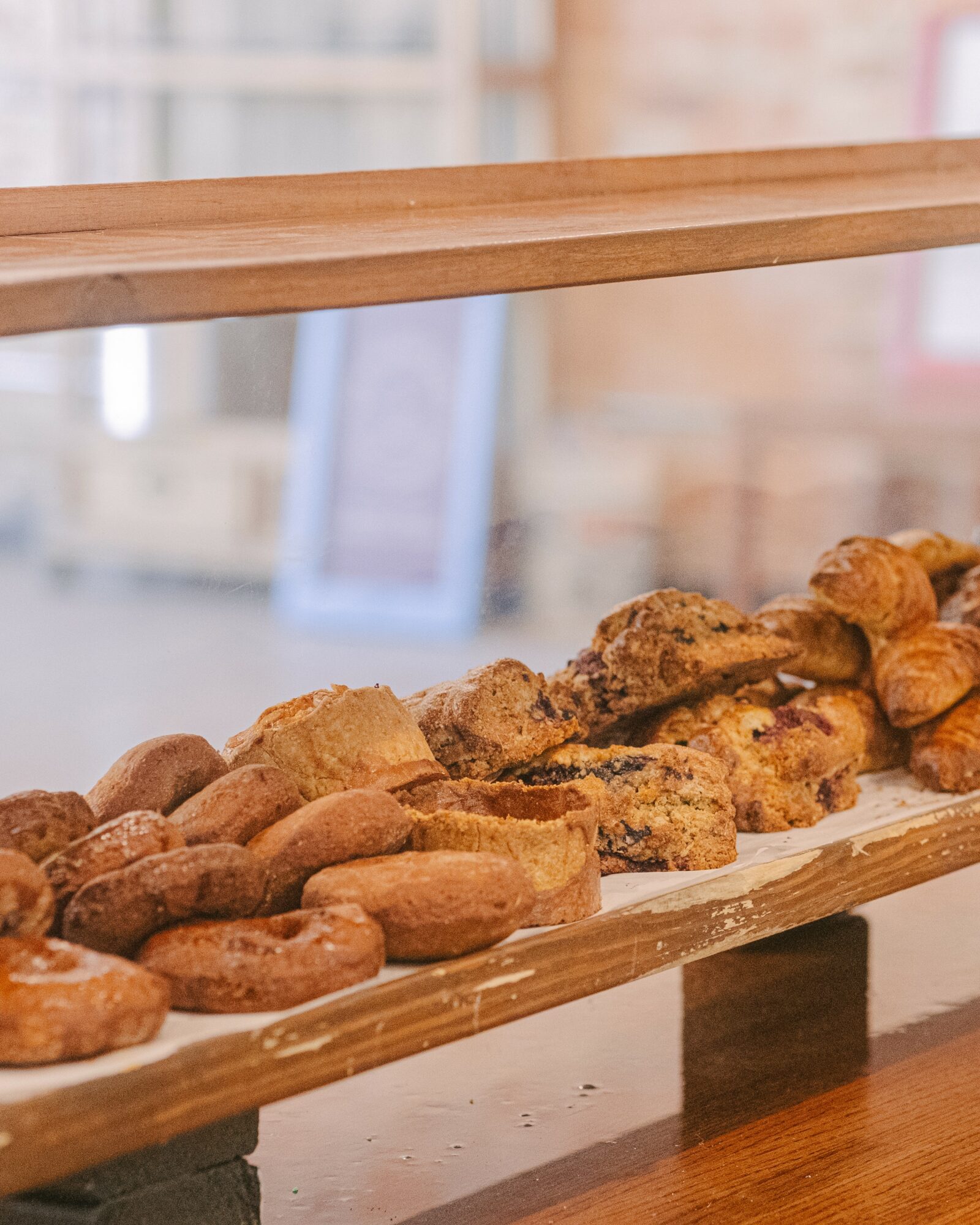 Wooden shelf with baked goods, blurred background of a bakery or cafe interior, warm lighting, and a framed picture.