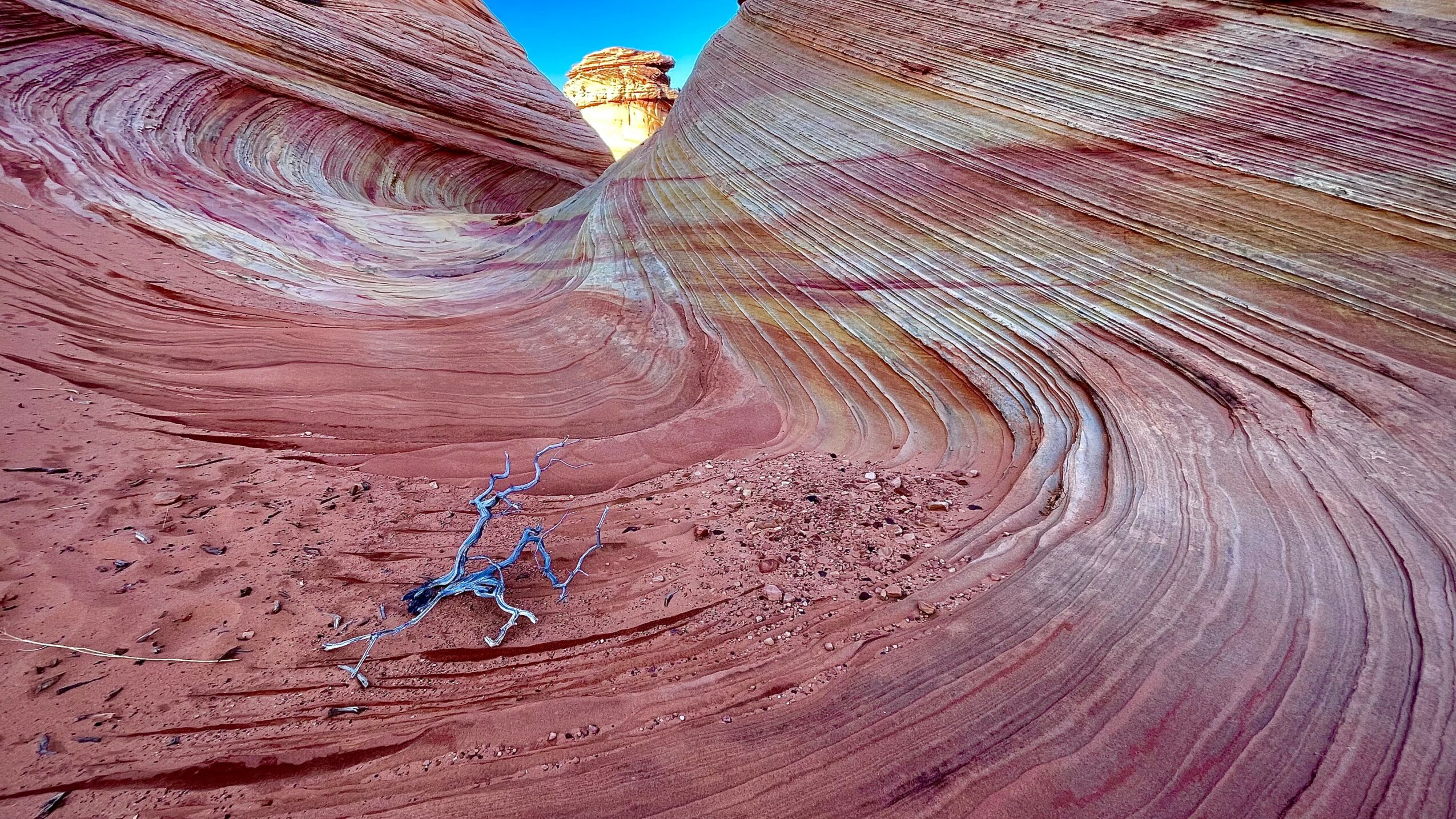 Person lying on colorful, layered rock formations with swirling patterns in a desert landscape.