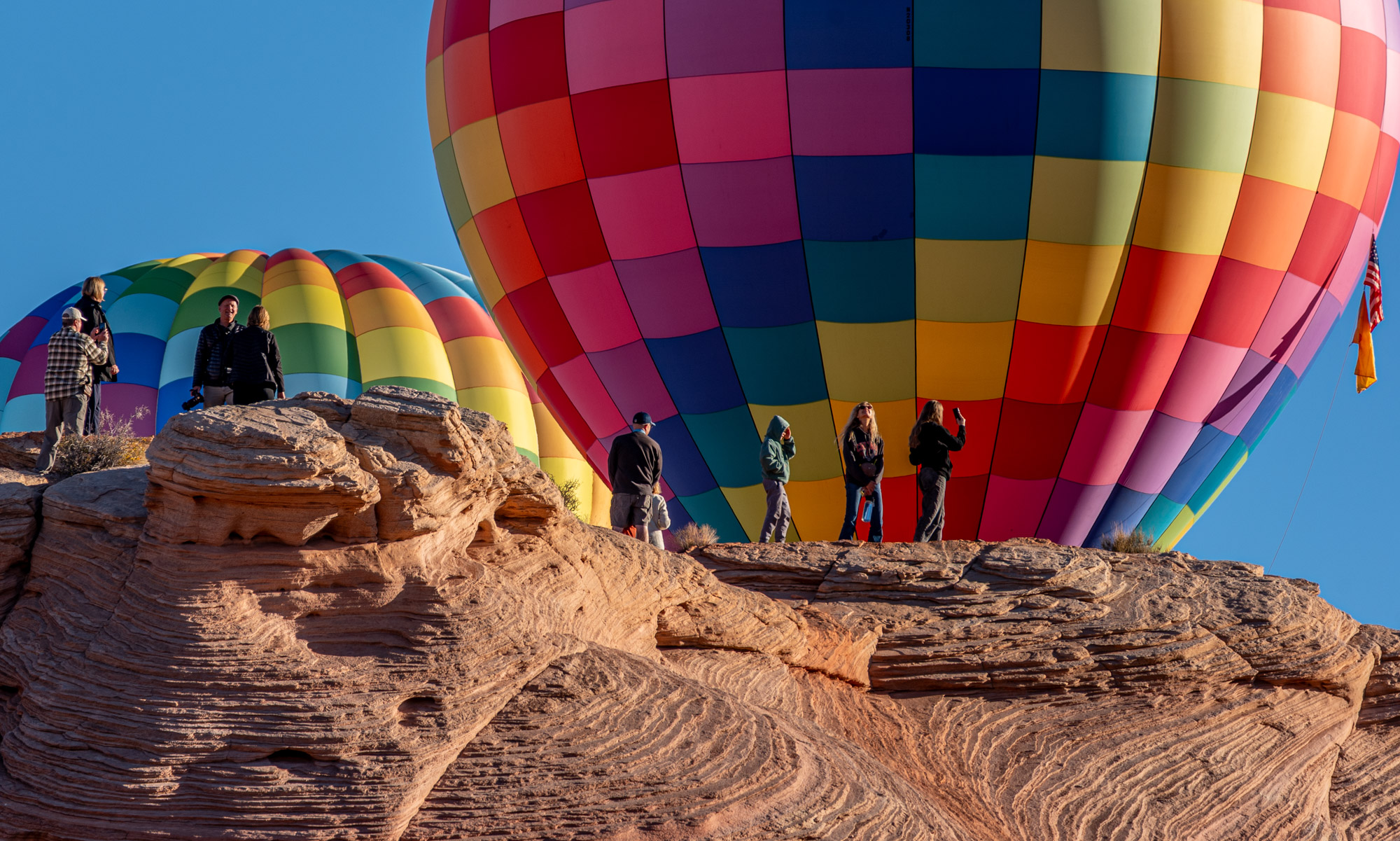 Colorful hot air balloons on rocky terrain with people preparing for flight, blue sky background.