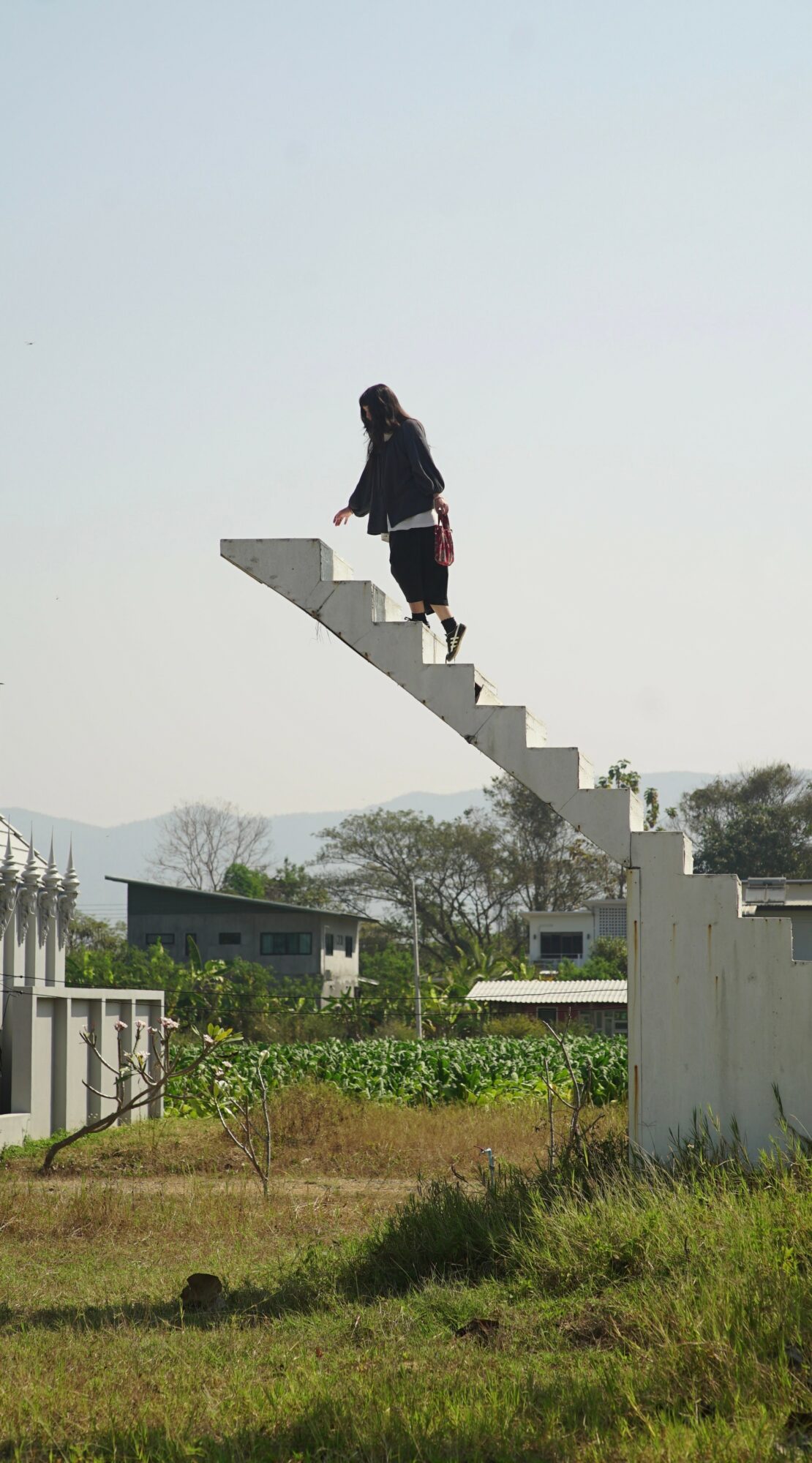 Person walking up a staircase suspended in the air outdoors, with trees and buildings in the background.
