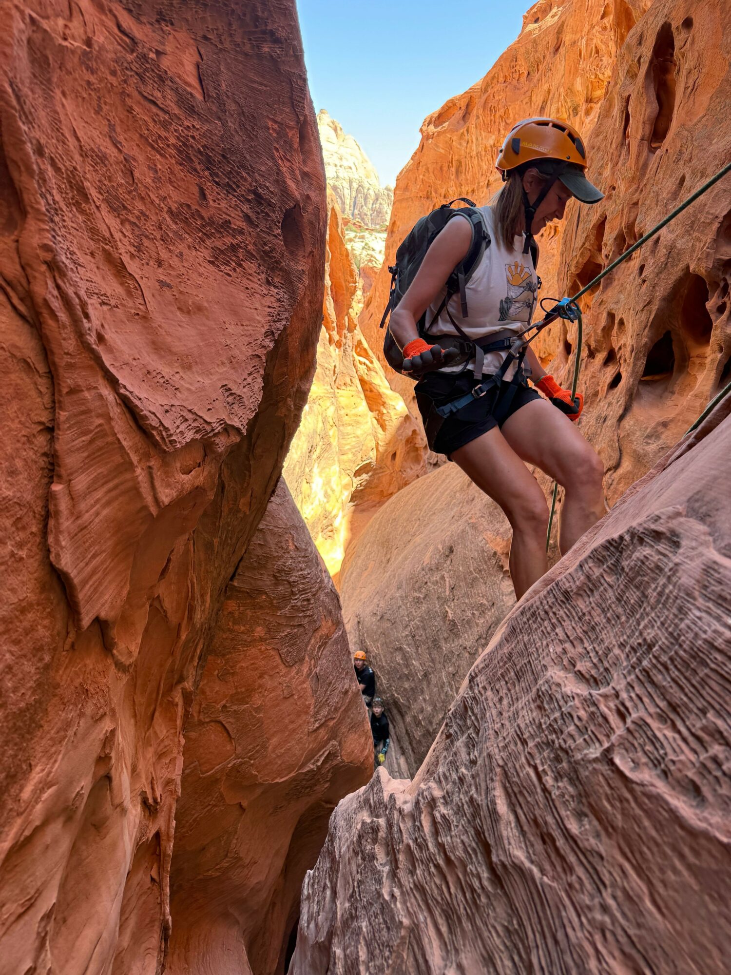 Person climbing a rock formation with a harness and helmet in a canyon landscape.