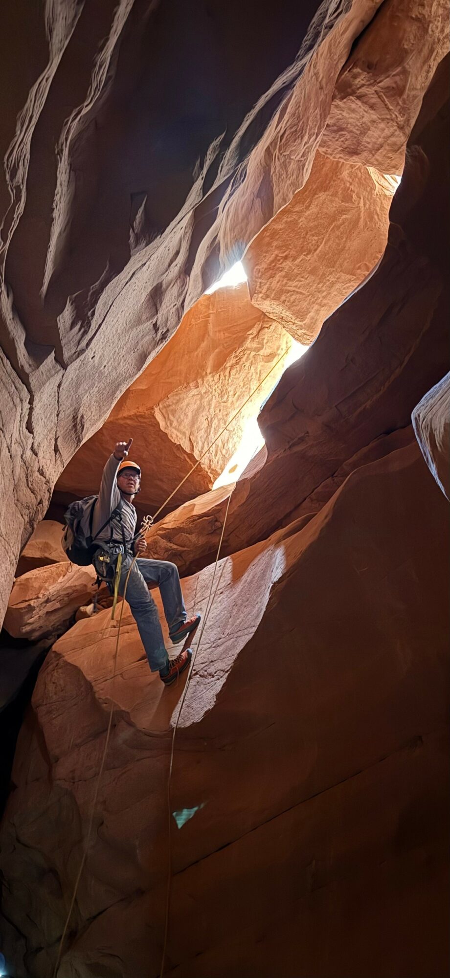 Person sitting on a rock inside a narrow canyon with sunlight shining through opening above.