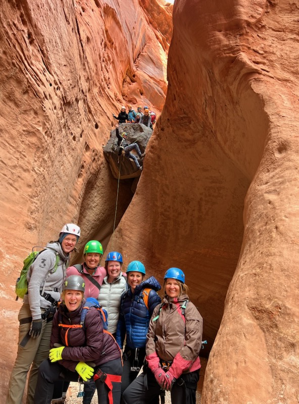 Group of five people in outdoor gear standing in a narrow canyon with red rock walls.