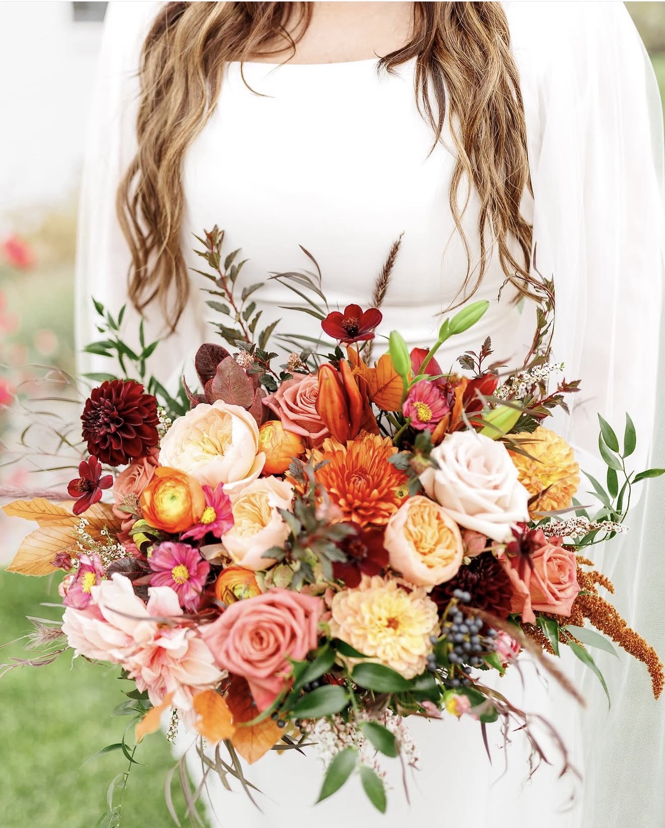 Person holding a large colorful bouquet of flowers, with long hair and a white dress, outdoors.