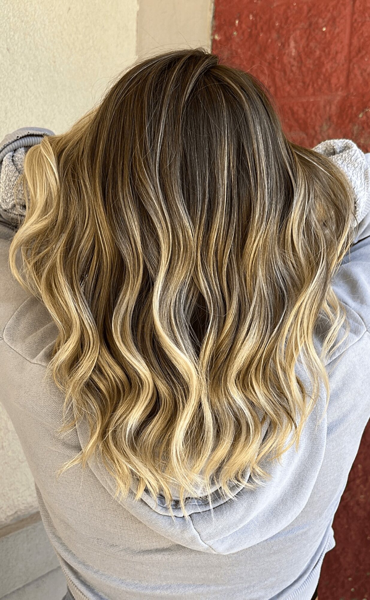 Top view of a person with long, wavy, blonde hair with darker roots, wearing a light-colored hoodie.