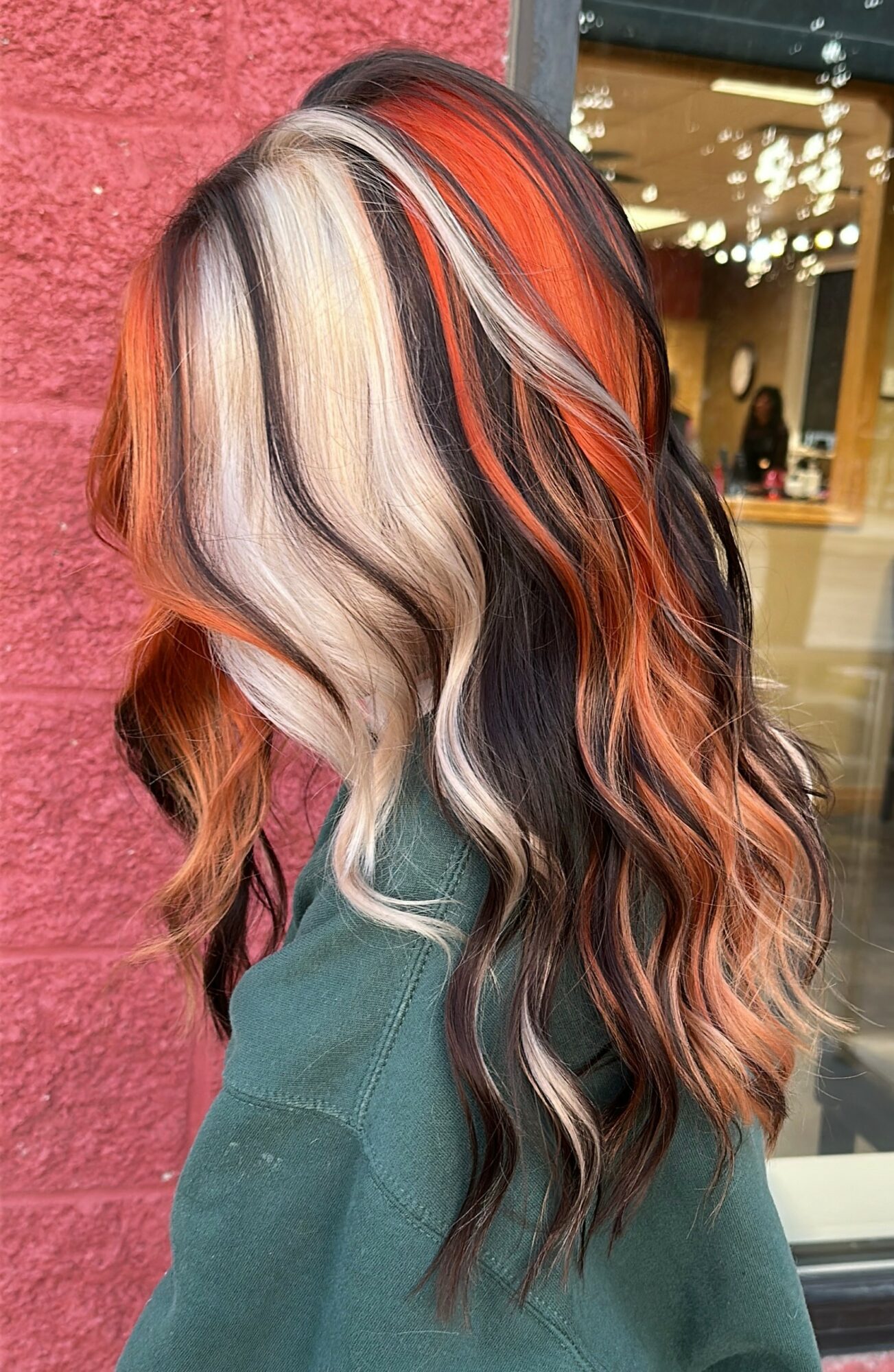 Side view of wavy hair with blonde, black, red, and copper streaks, styled in loose waves.