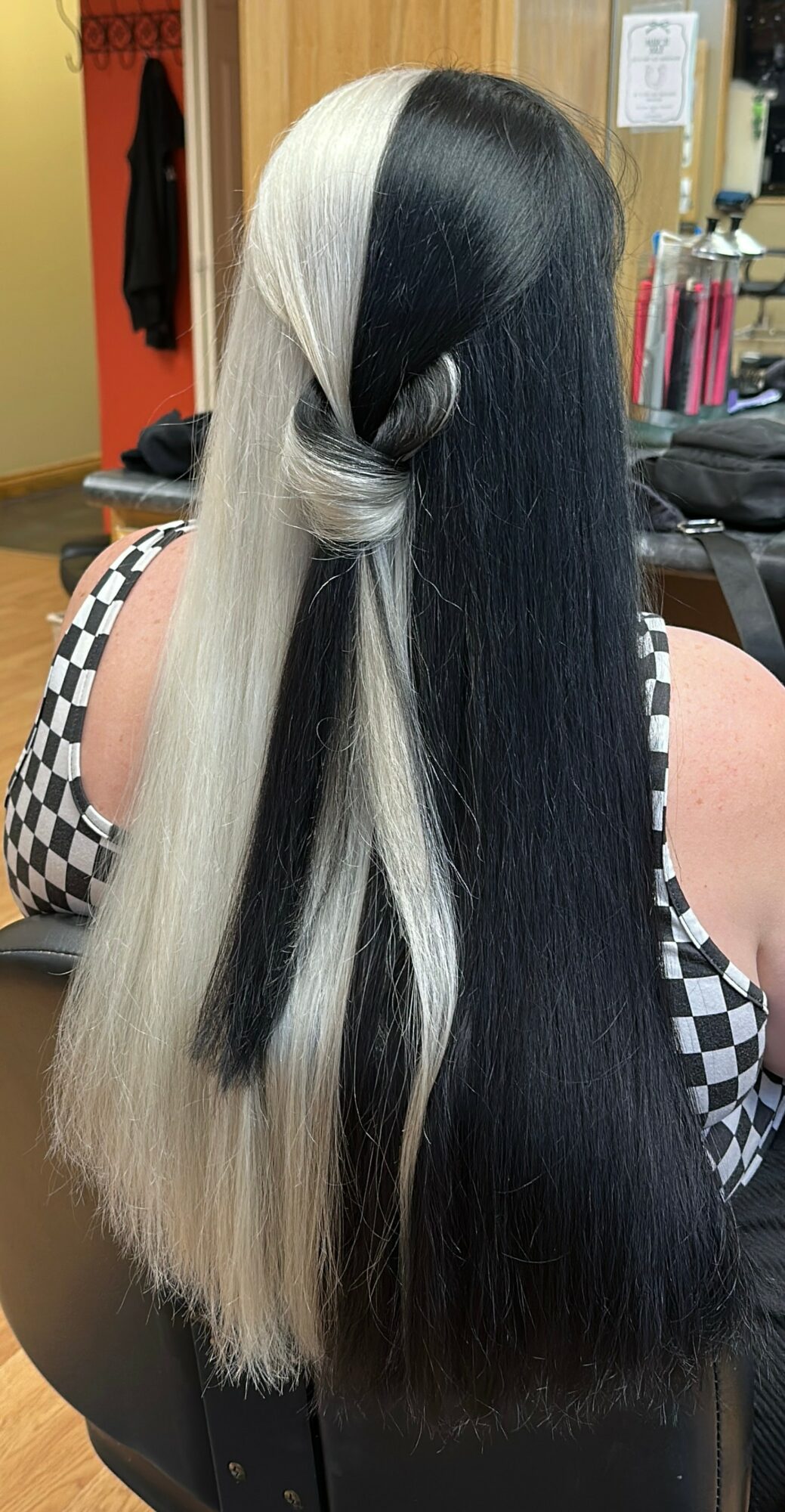 Person with long, black and platinum blonde hair styled with a twist, sitting in a salon chair.