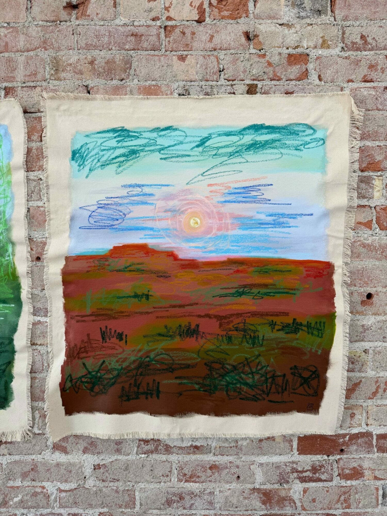 Two pieces of fabric with colorful abstract paintings, one with blue and pink, the other with green and brown, on a brick wall.