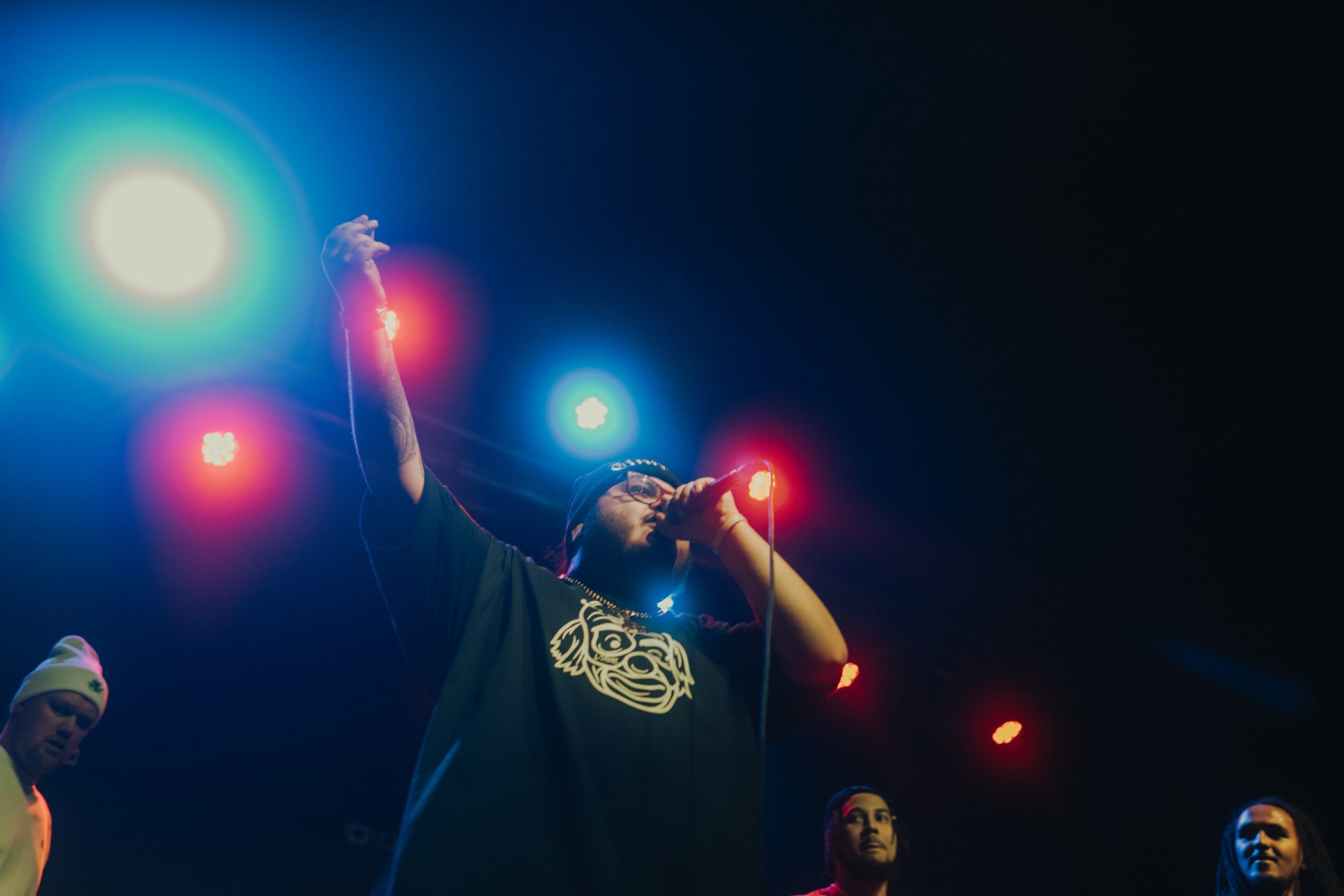 Person holding a lit sparkler on stage with bright lights and other people in the background.