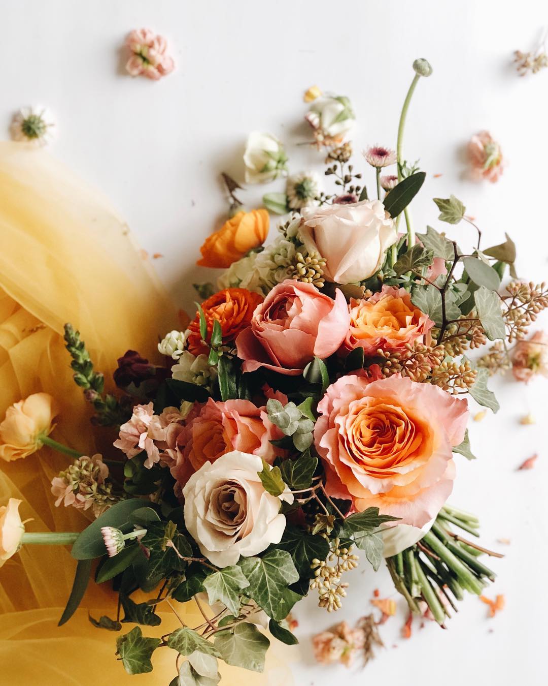 Bouquet of pink, white, and orange roses with greenery and small flowers on a white background.