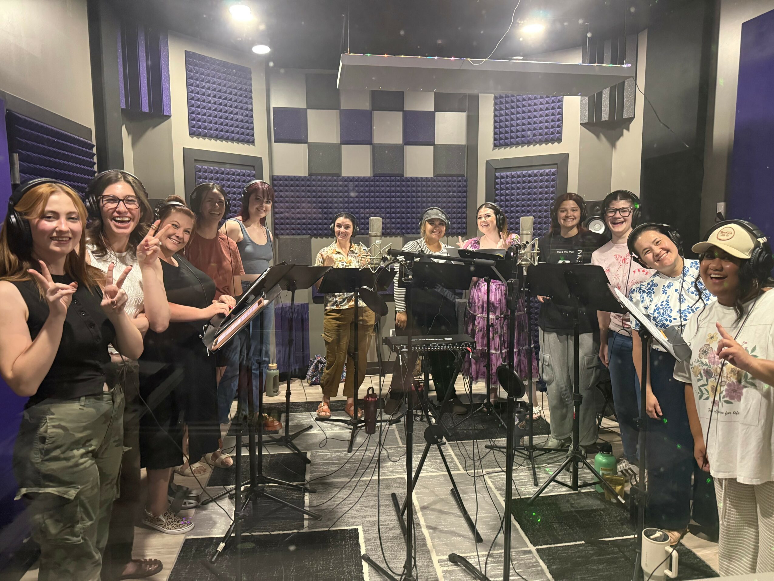 Group of people in a recording studio with microphones and soundproof walls, smiling and posing for the photo.