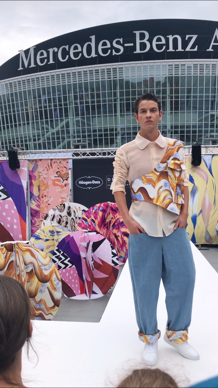 Person standing in front of colorful abstract sculptures outside Mercedes-Benz Arena, with a modern glass building in background.