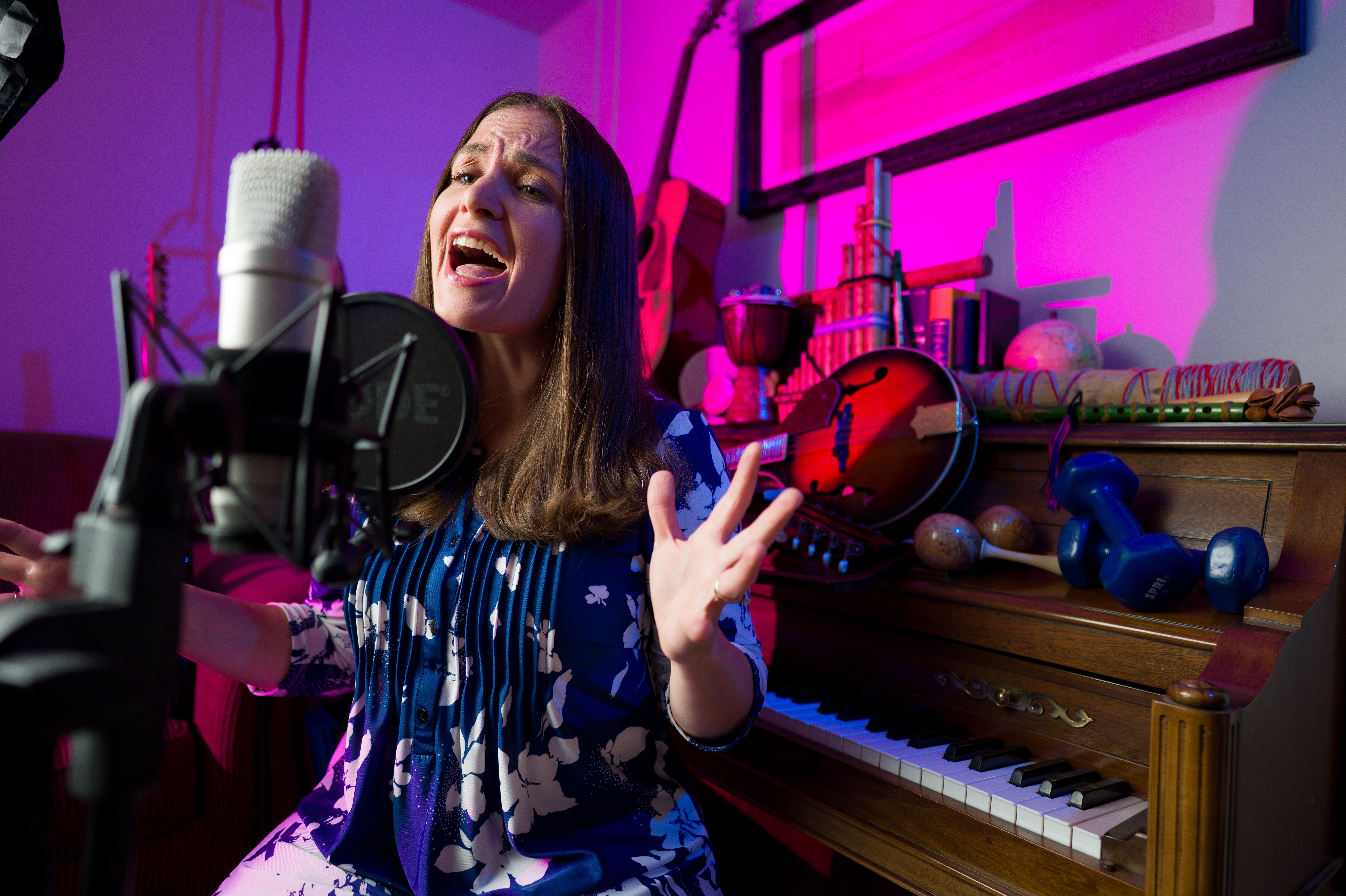 Woman singing passionately into a microphone in a colorful room with musical instruments and equipment