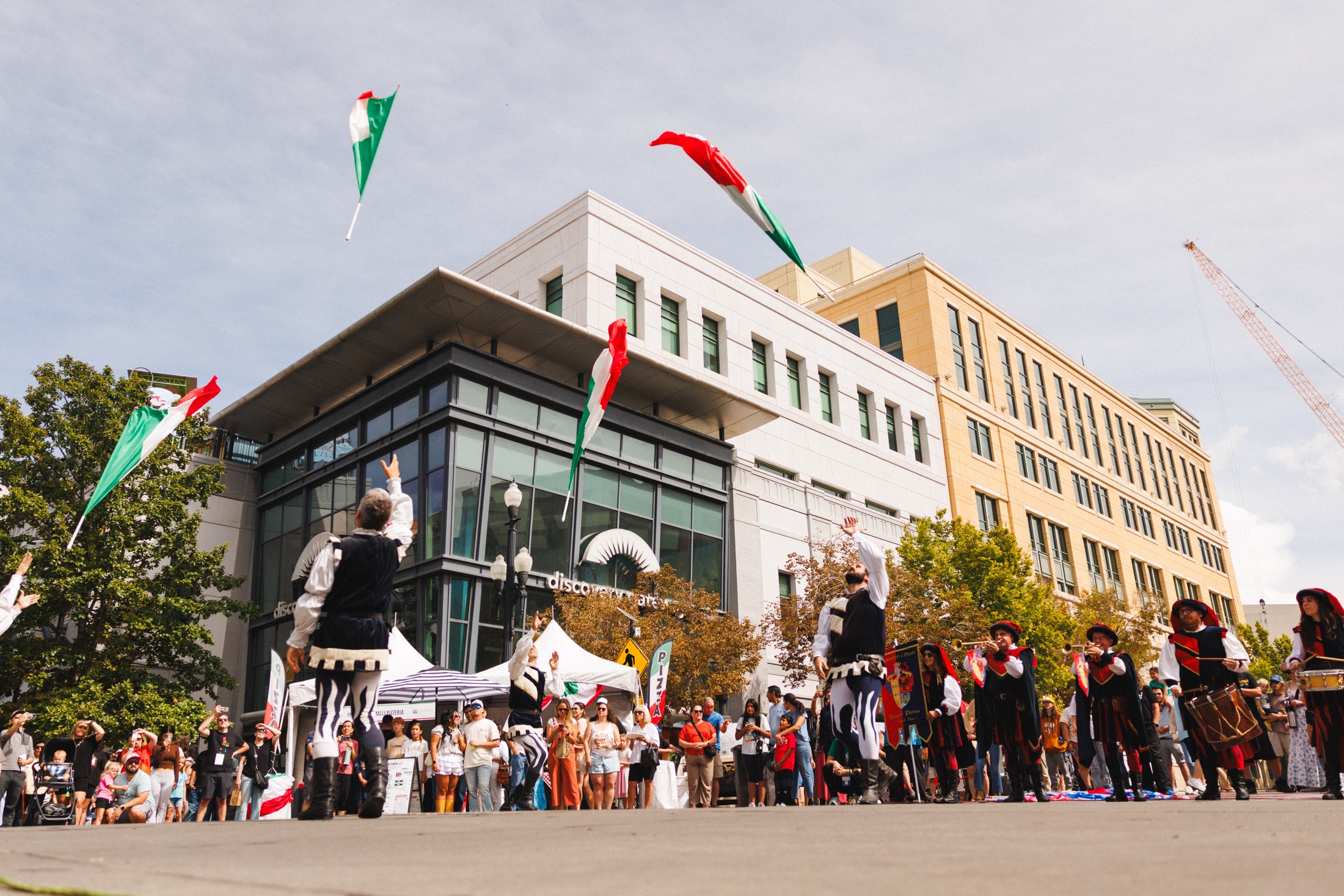 Crowd gathered outdoors in front of modern buildings during a festive event with flags and decorations.