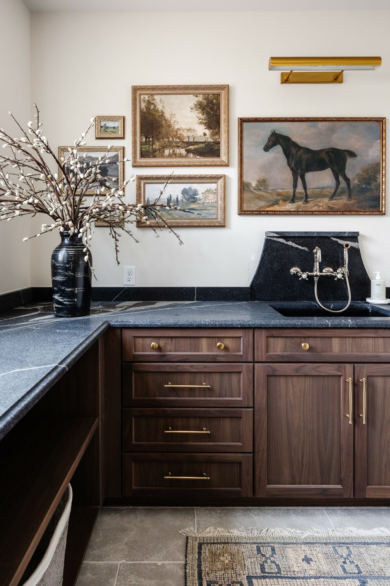 Kitchen with dark wood cabinets, black countertop, and a wall decorated with framed landscape paintings and a horse picture.