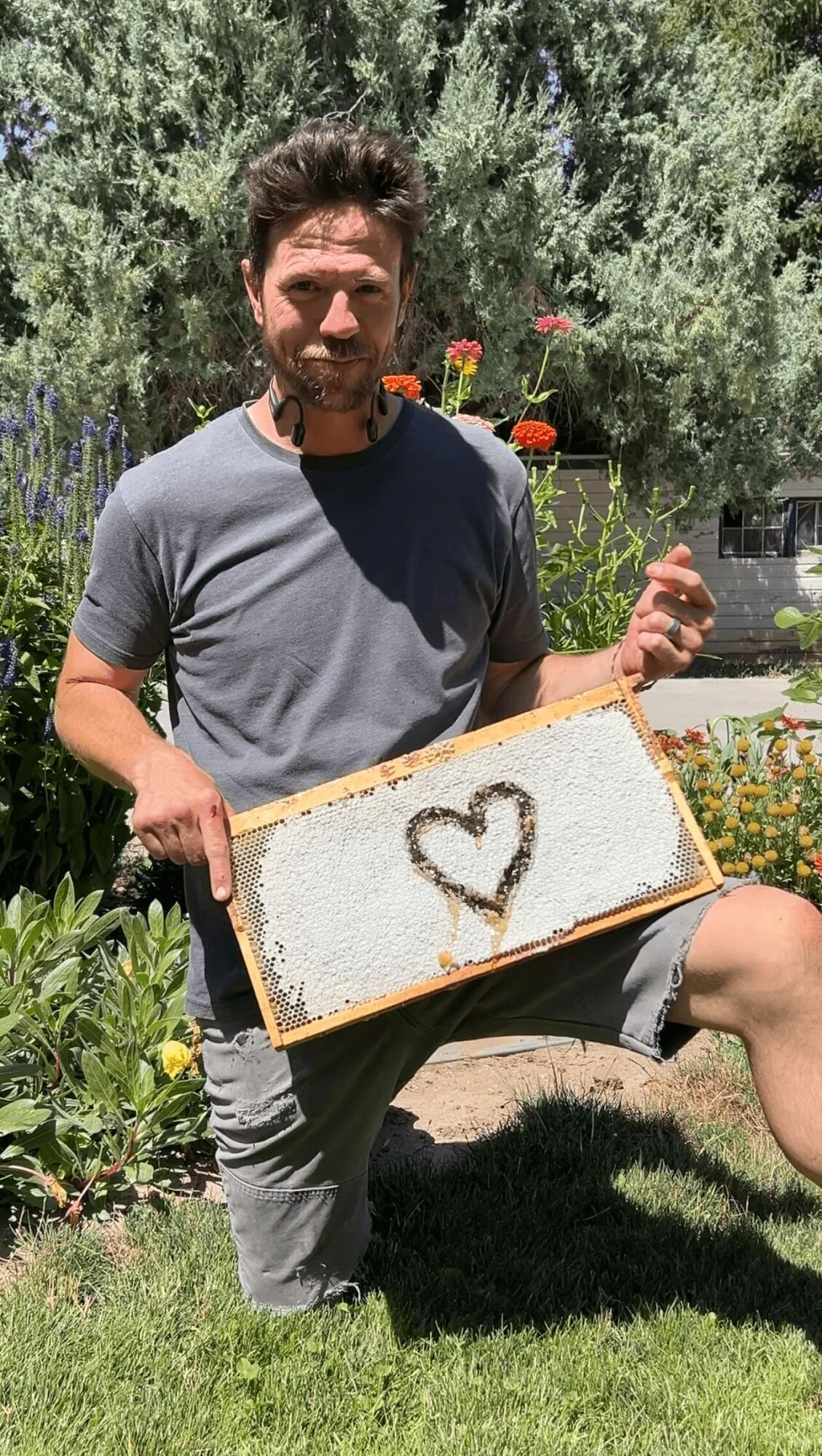 Man with beard holding a sign with a heart drawn on it in a garden with flowers and greenery