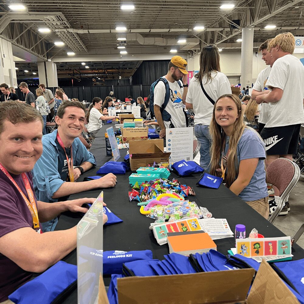 People sitting at a table with colorful items in an indoor event space, smiling and engaging with each other.