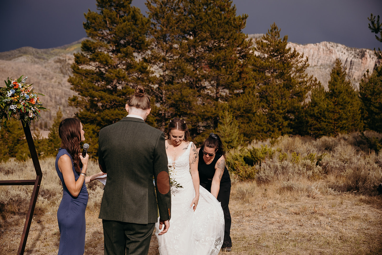 People gathered outdoors, with trees and mountains in the background, during a wedding ceremony or celebration.