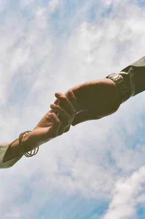 Two people hold hands against a cloudy sky background.