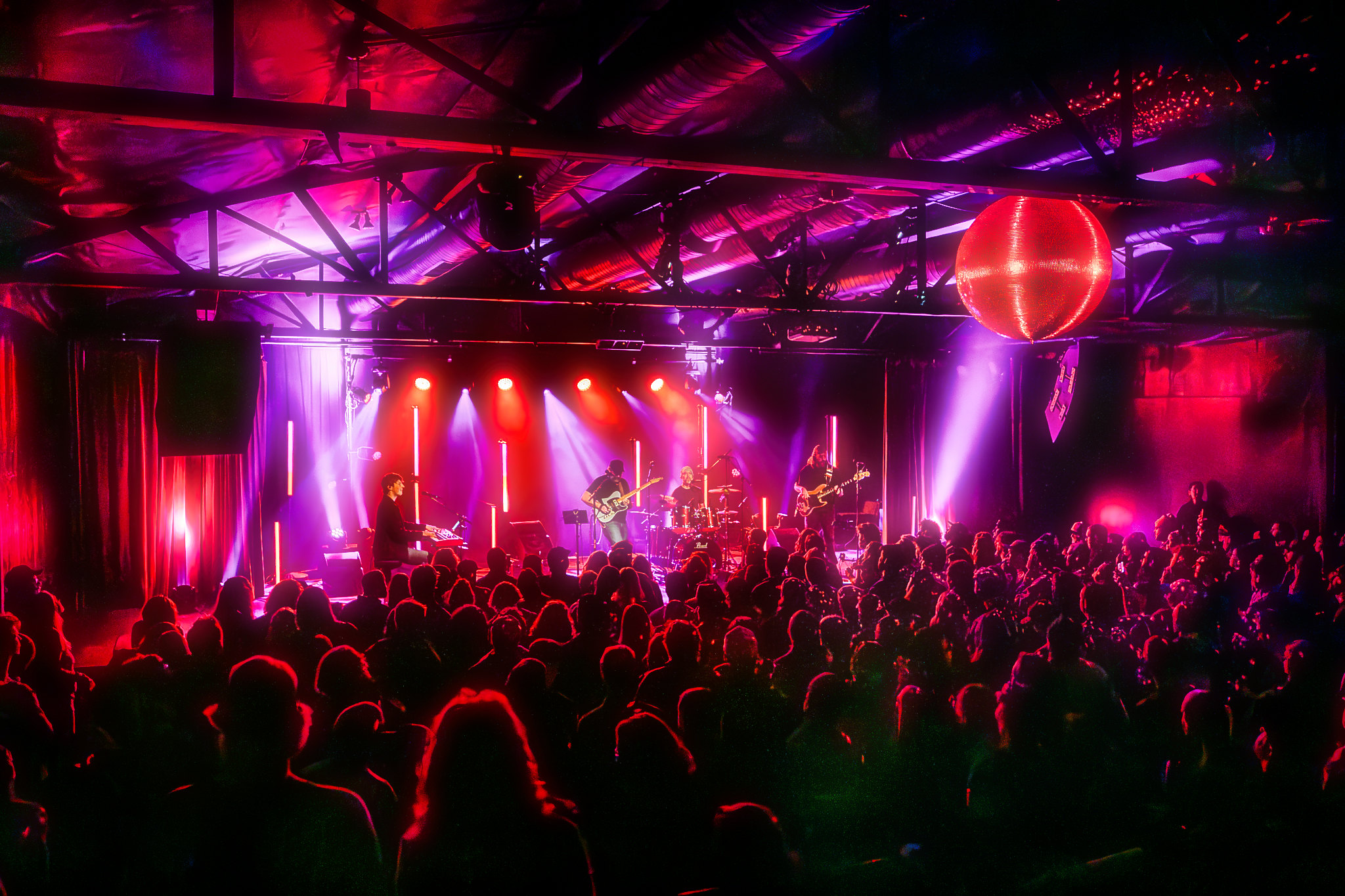 Concert stage with colorful lighting and a large audience, performer playing guitar, vibrant atmosphere.
