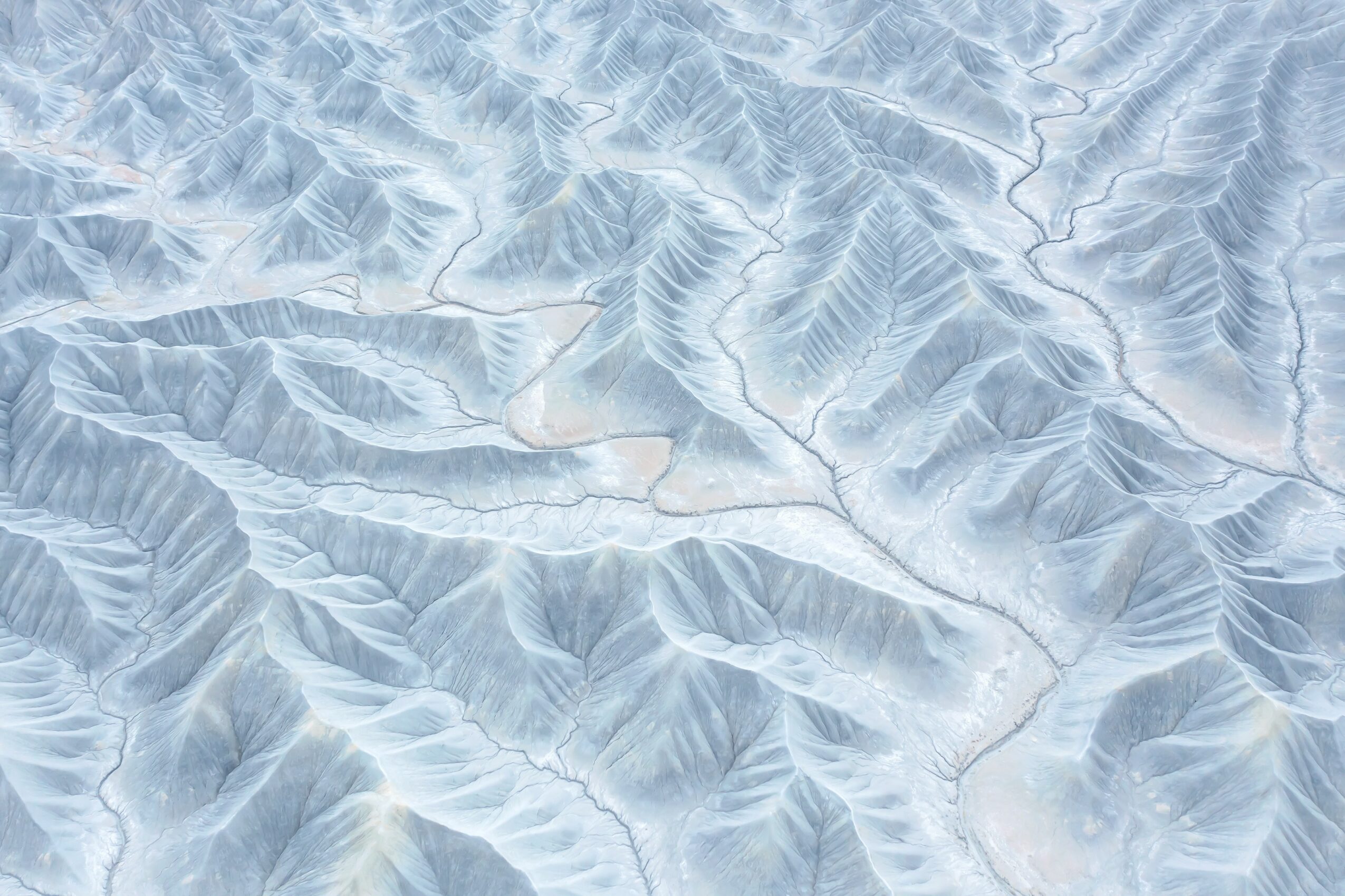 Aerial view of snow-covered mountain ridges and valleys with visible crevices and shadows.