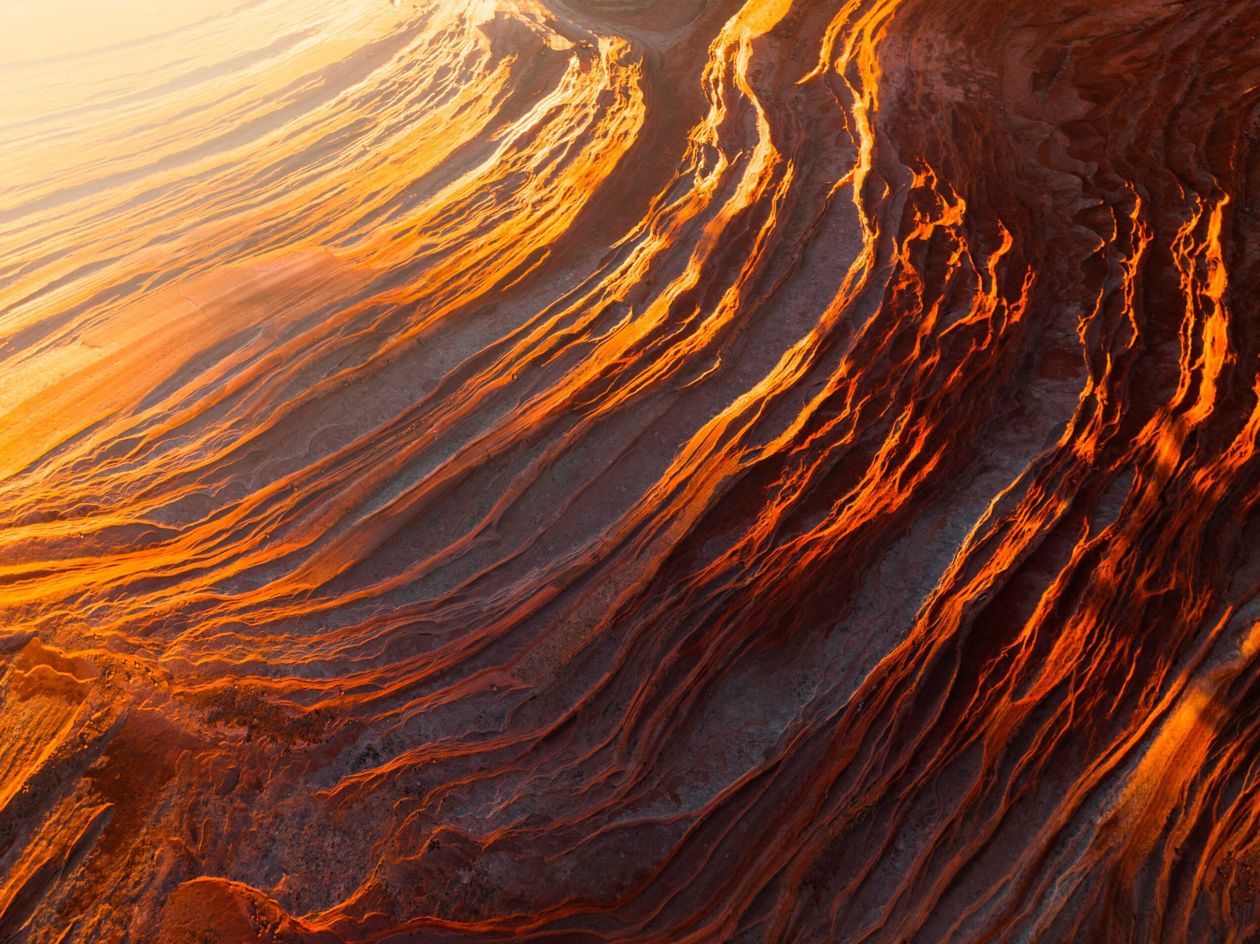 Close-up of layered rock formations with orange and dark brown colors, illuminated by sunlight.