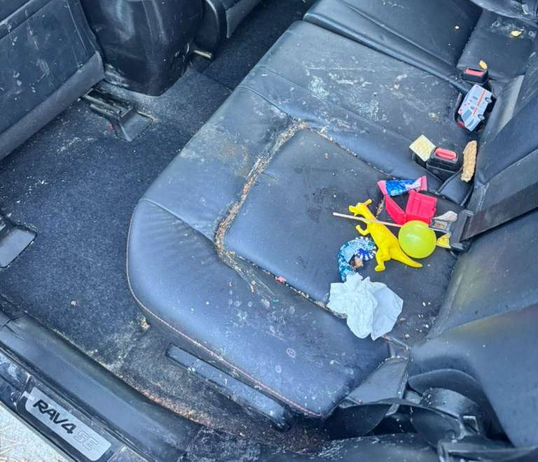 Dirty car back seat with trash, toys, and debris scattered on the seat and floor.