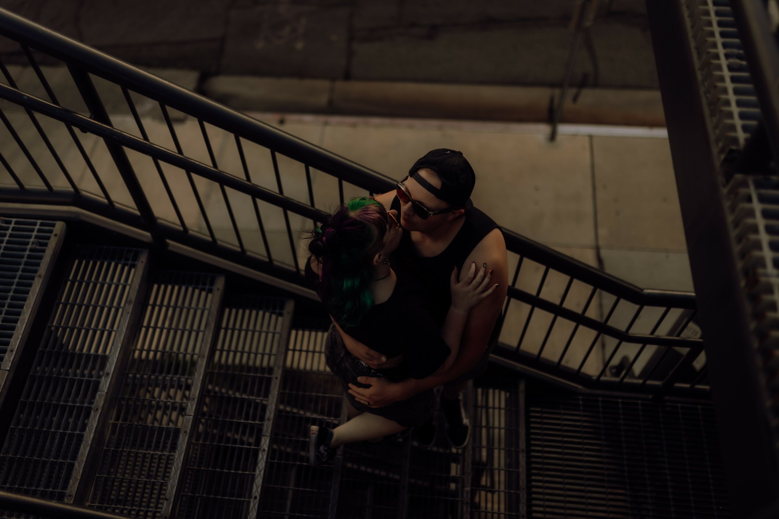 Person with glasses and a black shirt holding a small dog on a staircase, viewed from above.