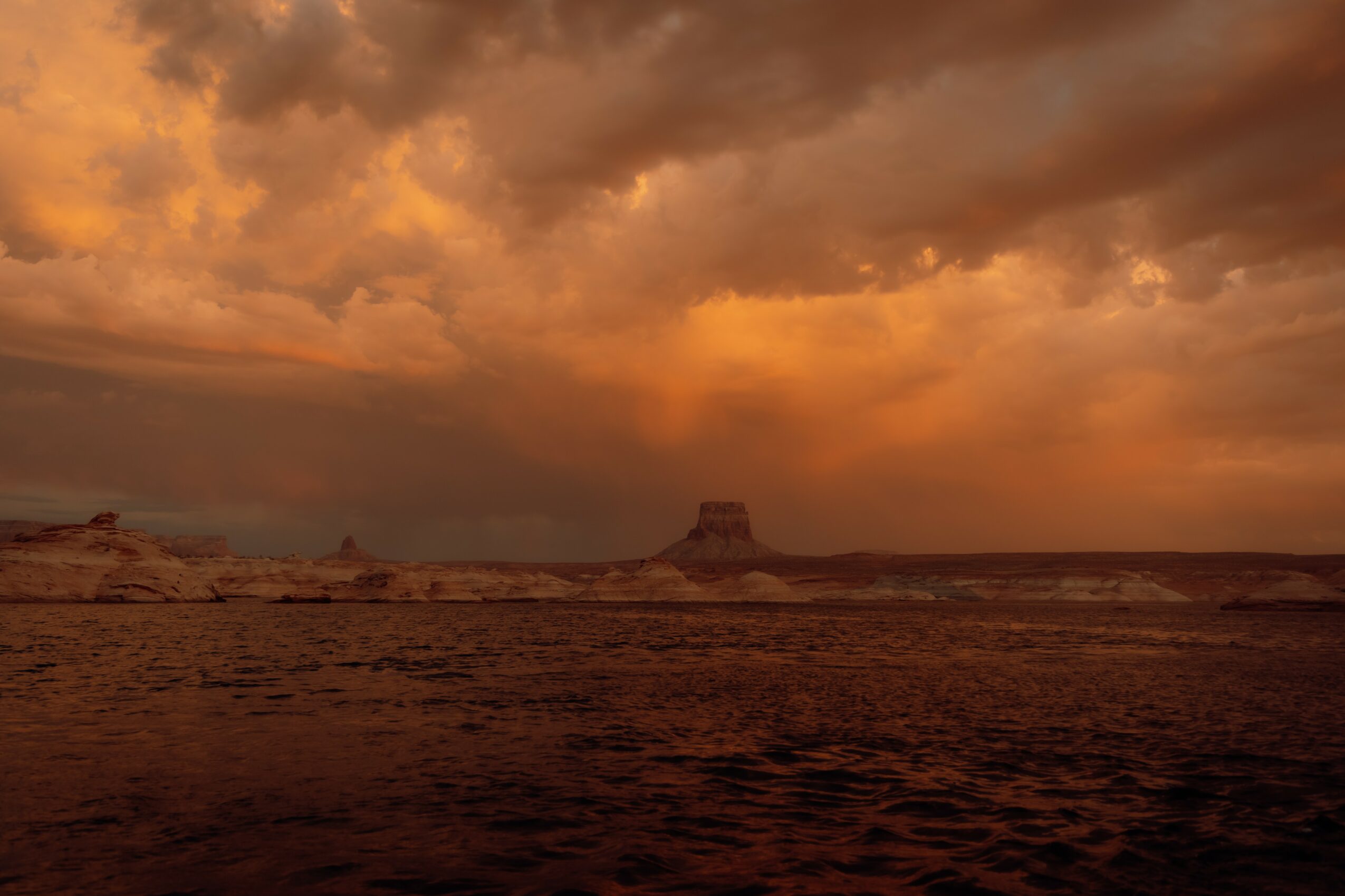 Desert landscape with a flat-topped mesa under a dramatic, cloudy sky at sunset or sunrise.