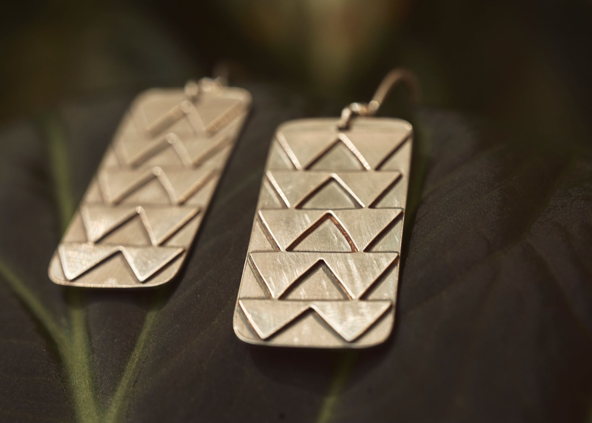Pair of rectangular metallic earrings with zigzag pattern, one with hook, on dark background.