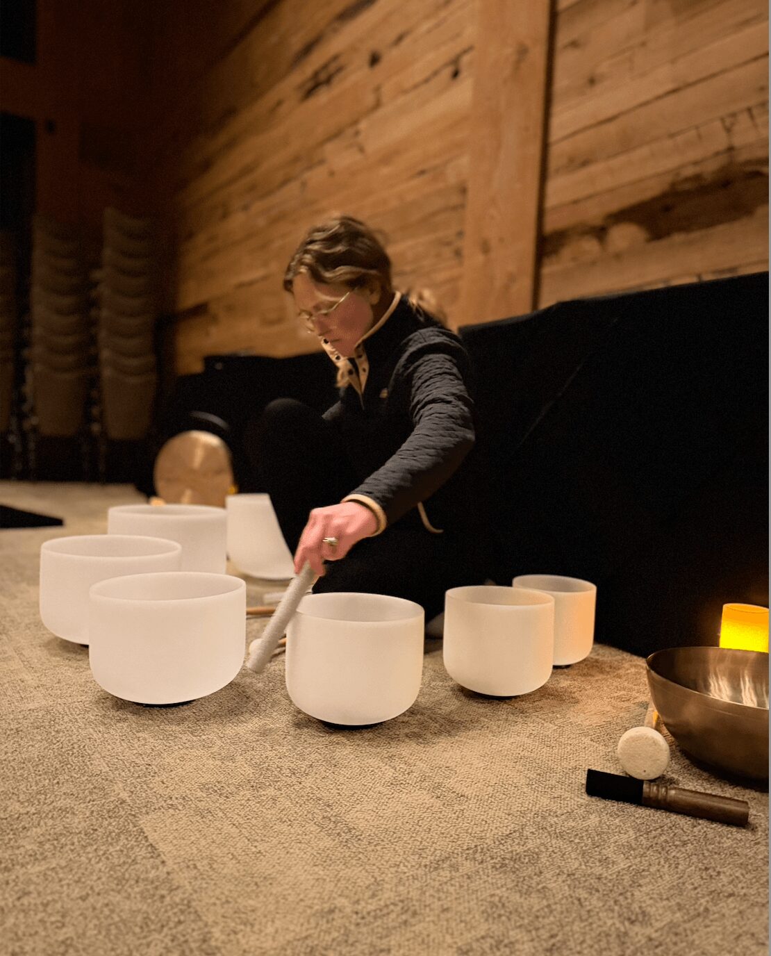 Child playing with white bowls on a table in a wooden room, wearing glasses and a dark sweater.