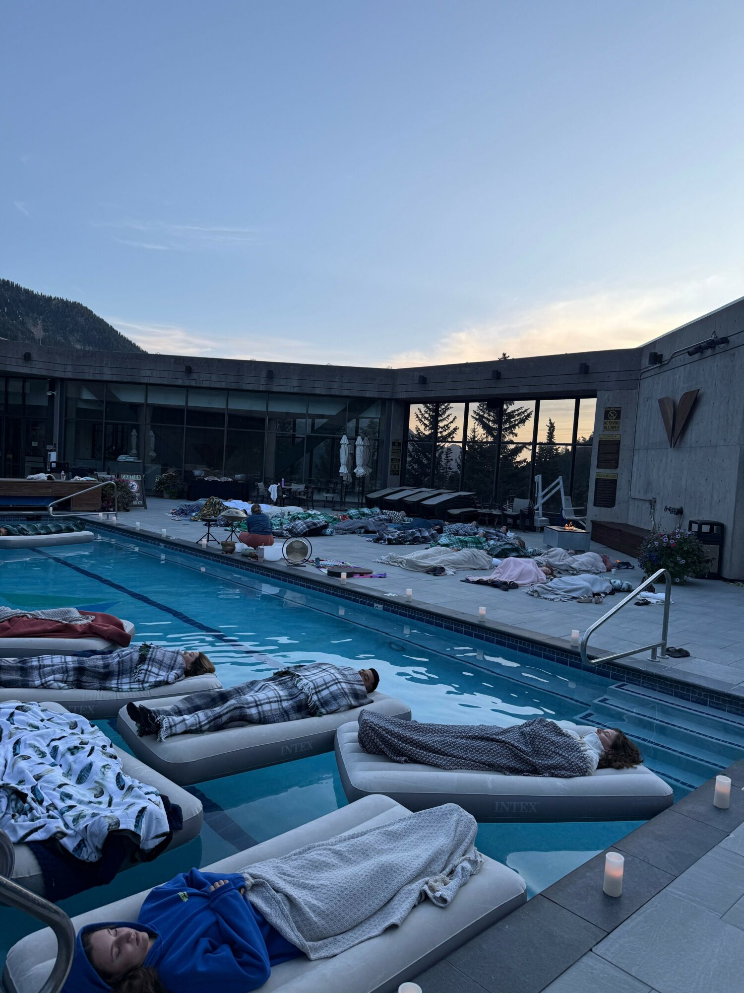 Poolside scene with towels and clothes on the edge, pool water, and a building in the background.