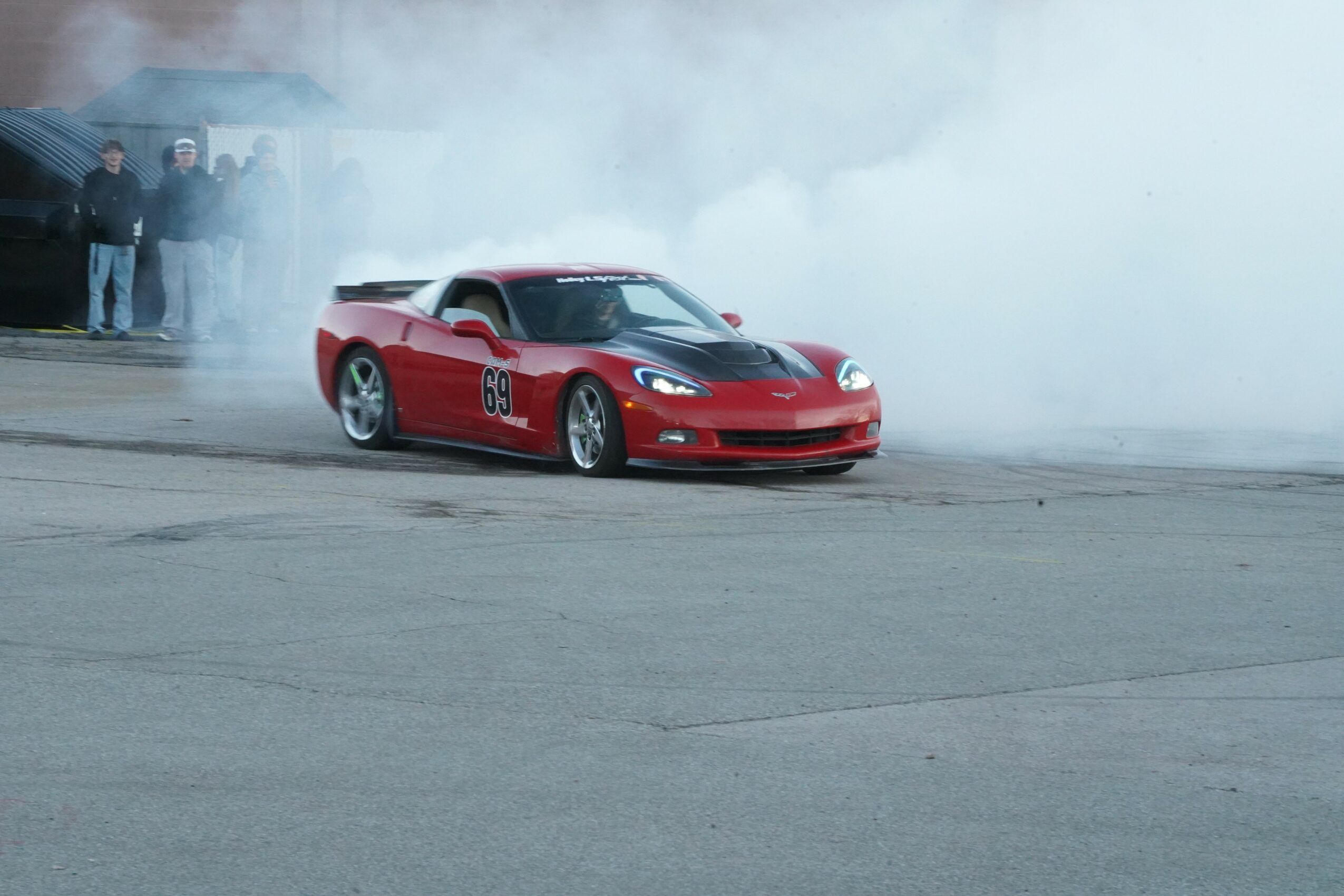 Red sports car drifting on a track with smoke and spectators in the background.
