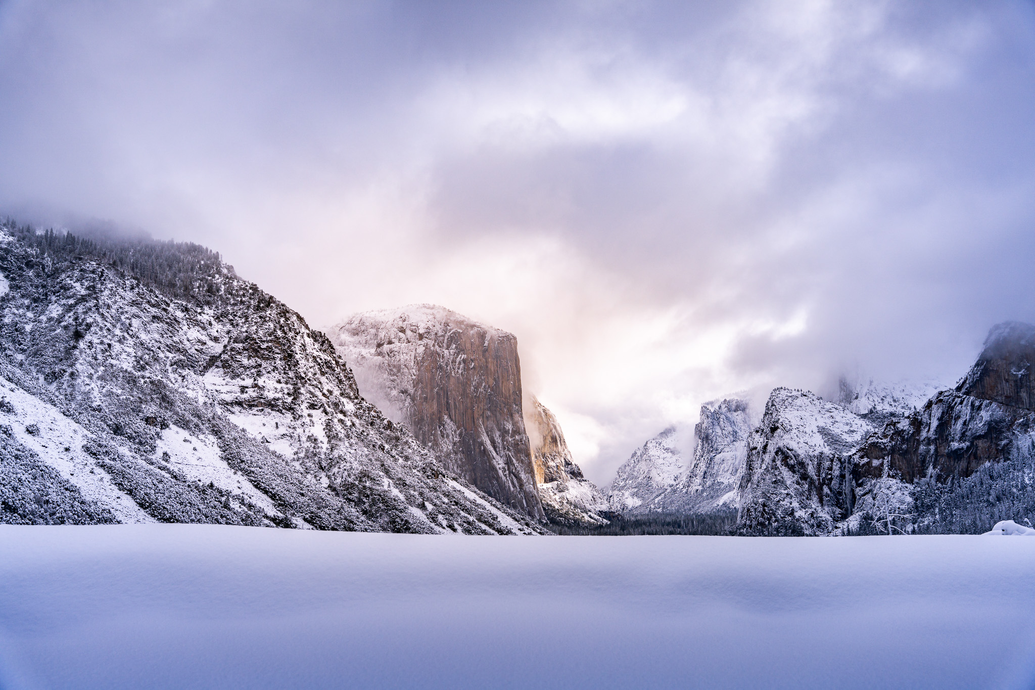 Snow-covered landscape with mountains and cloudy sky, possibly a winter scene.