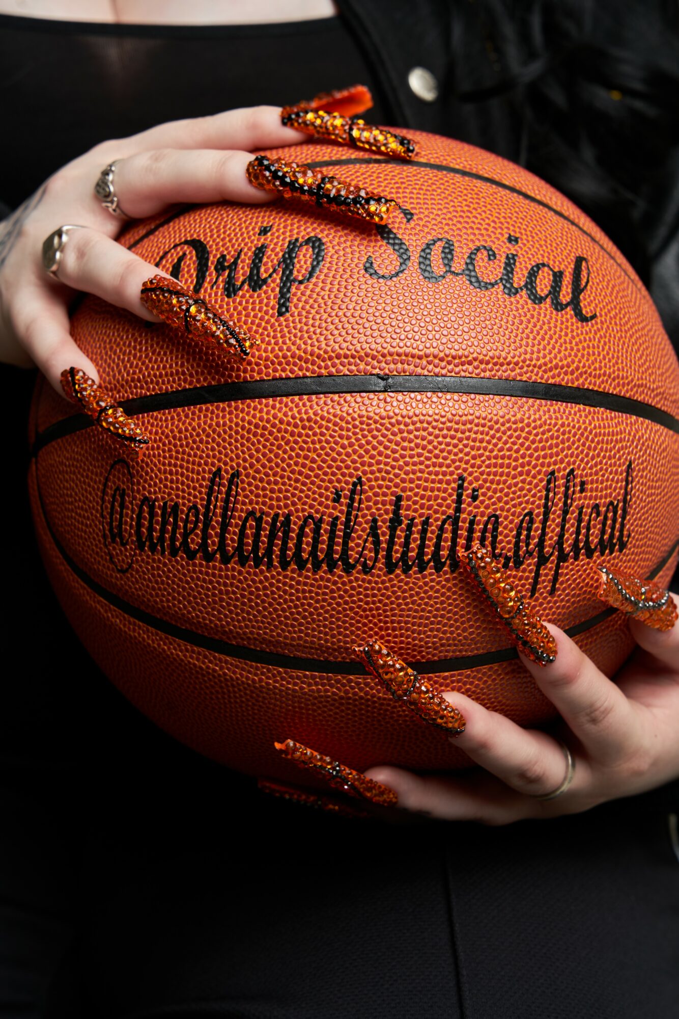 Person holding a basketball with long, decorated nails and rings, with handwritten text on the ball.