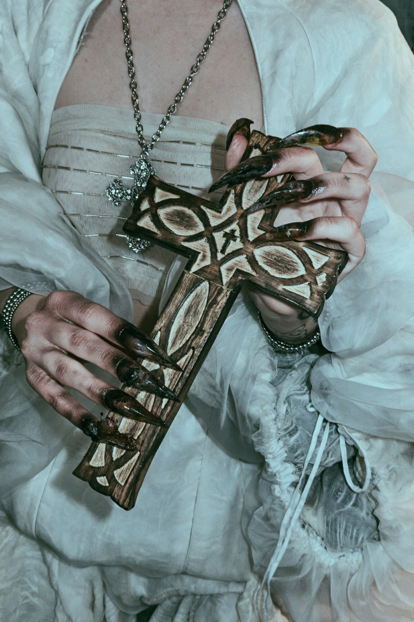 Person holding a large wooden cross with intricate designs, wearing dark gloves and layered clothing.