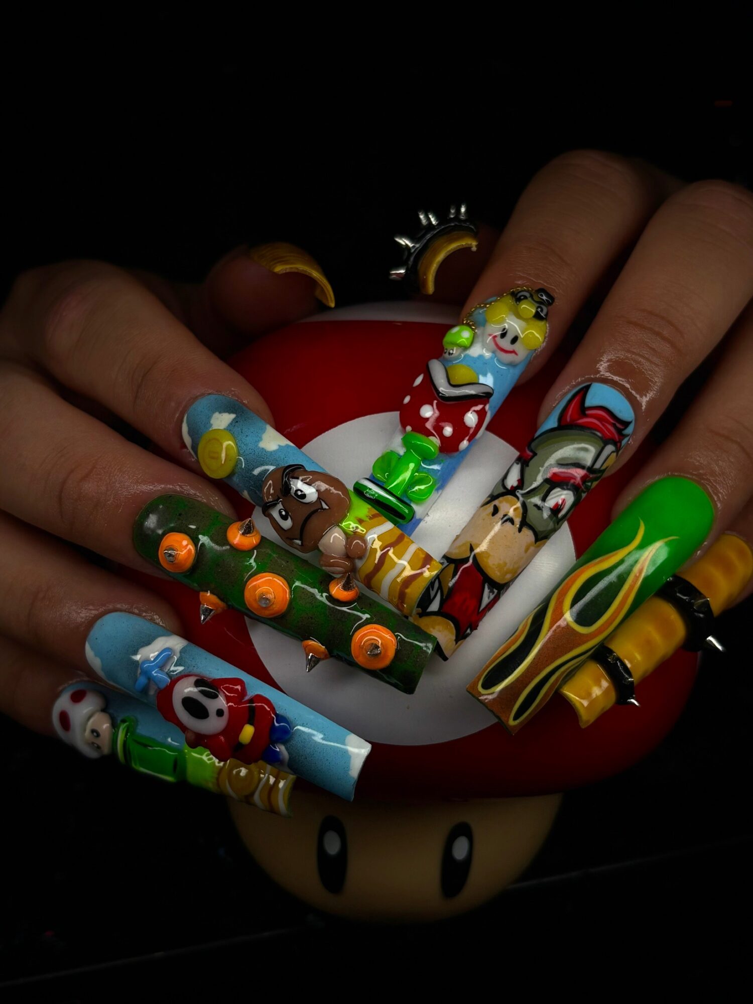 Hands with decorated nails holding a red and white object, with colorful cartoon character nail art and rings.