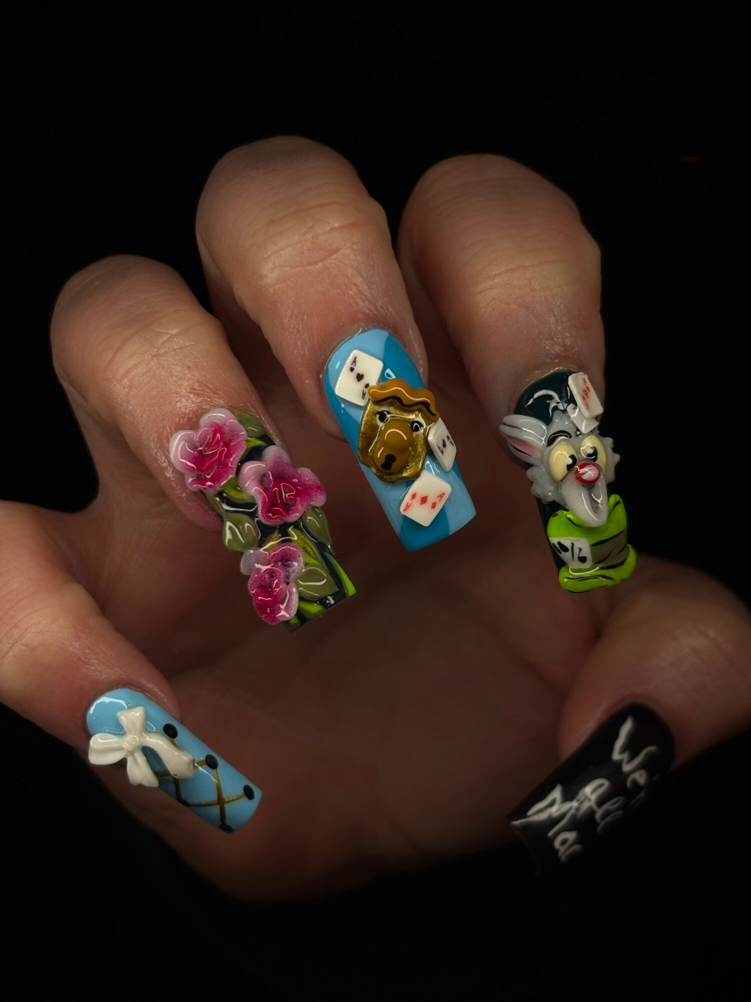 Hand with decorated nails featuring pink roses, a teddy bear, a unicorn, and a windmill design.